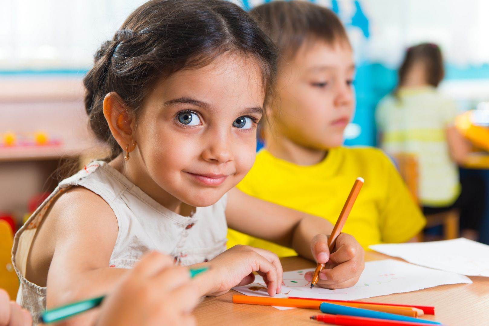 A little girl is sitting at a table drawing with colored pencils