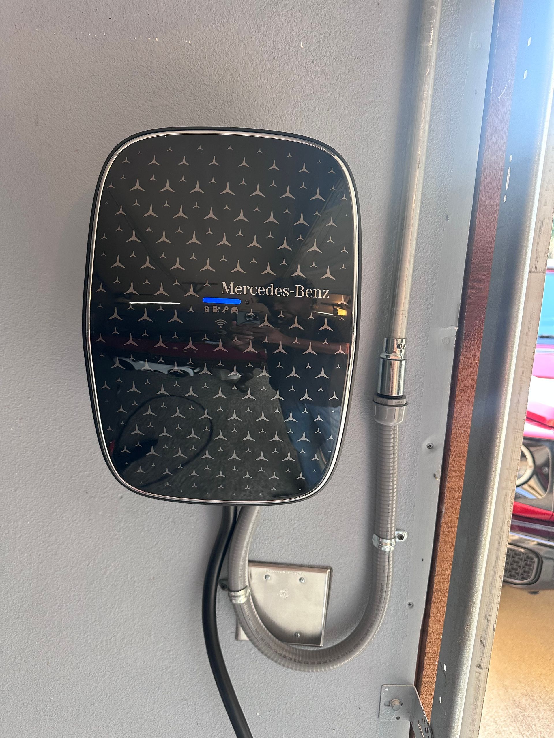 Black electric vehicle charger mounted on a gray wall with a flexible conduit.