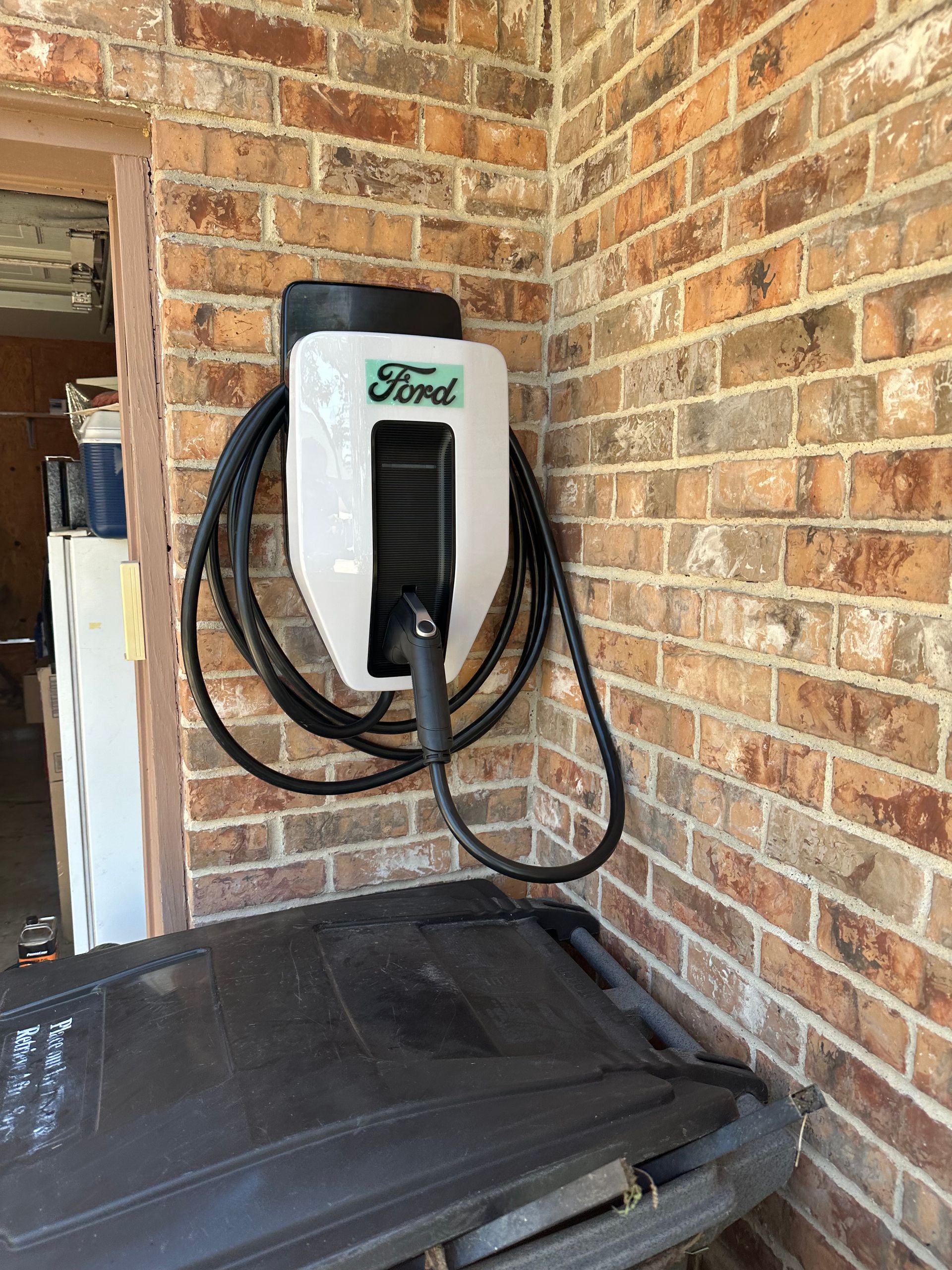 Ford electric vehicle charger mounted on a brick wall, with a charging cable hanging down.