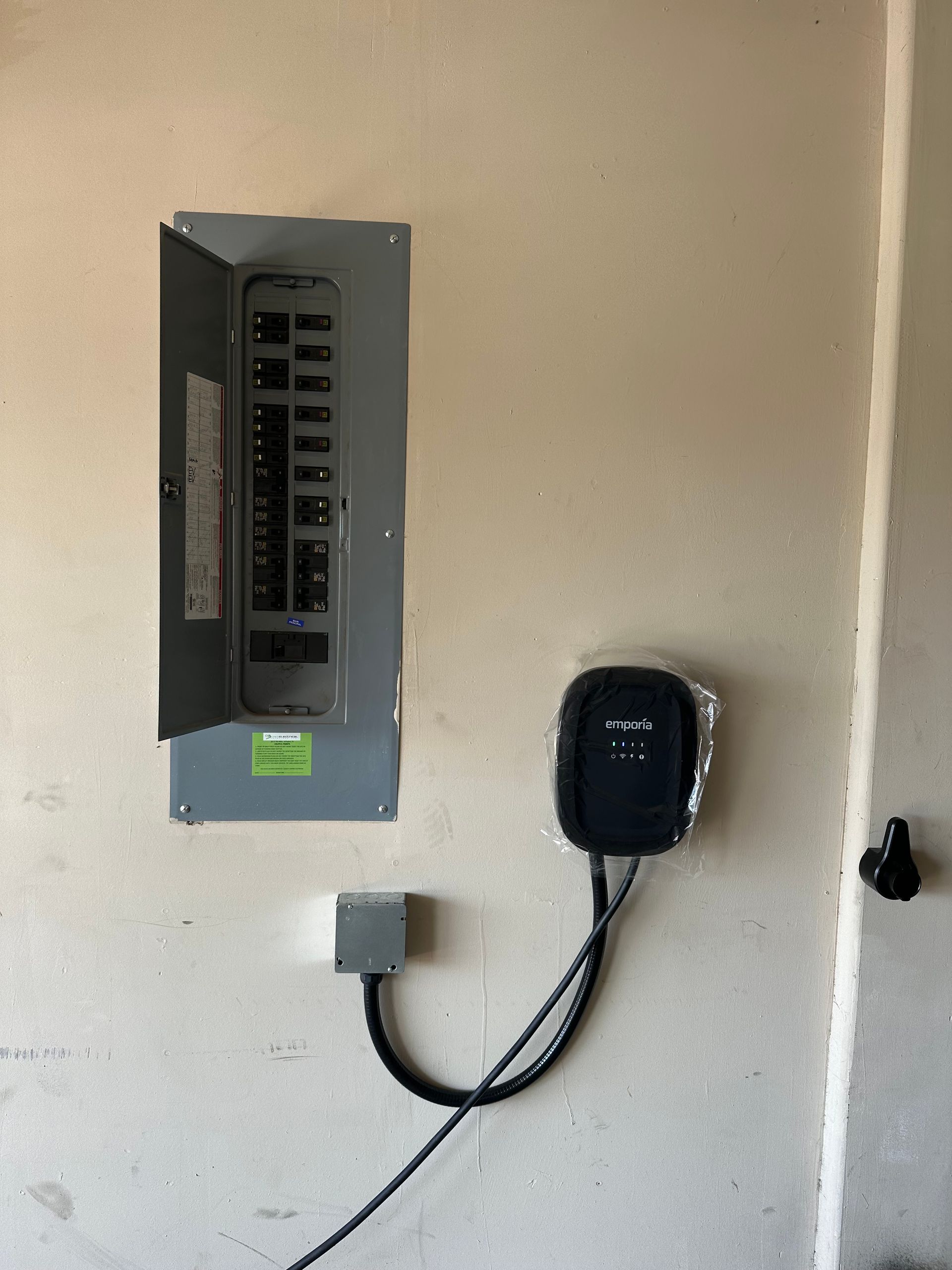 Electrical panel and EV charger on a beige wall, with connected wires.
