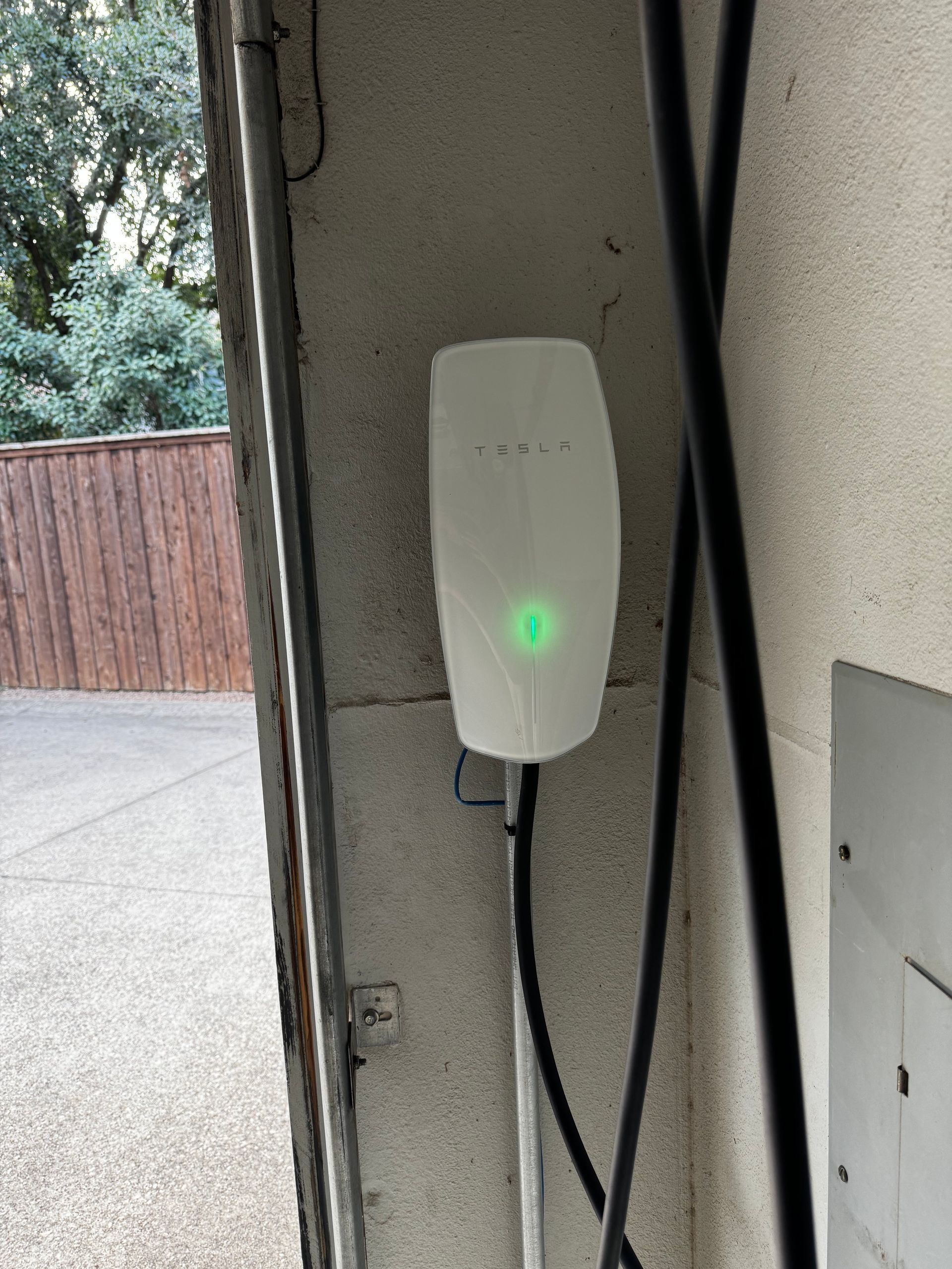 White EV charger with a green light mounted on a concrete wall, outdoors.