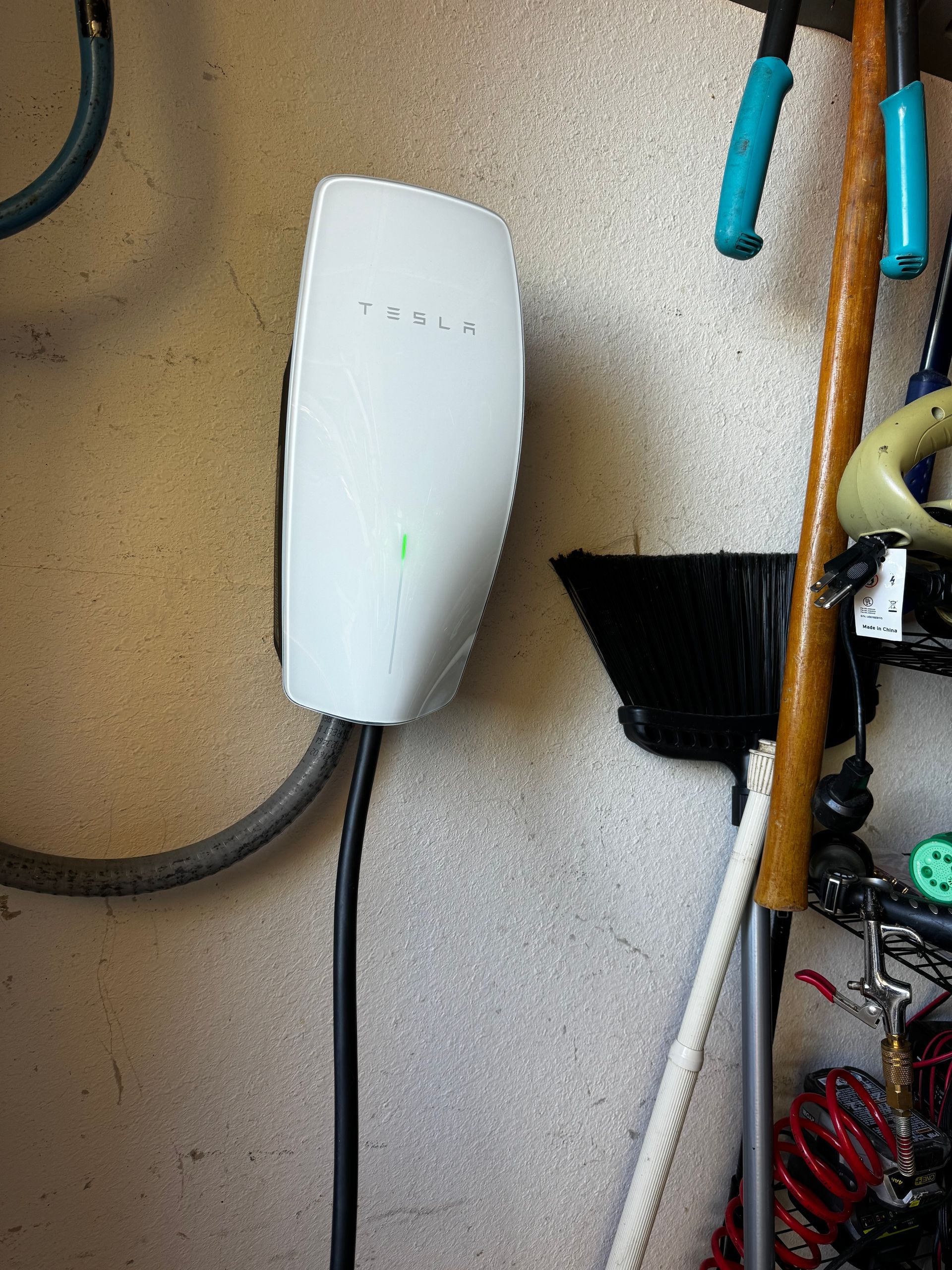 White Tesla charger mounted on a garage wall, cable hanging down.