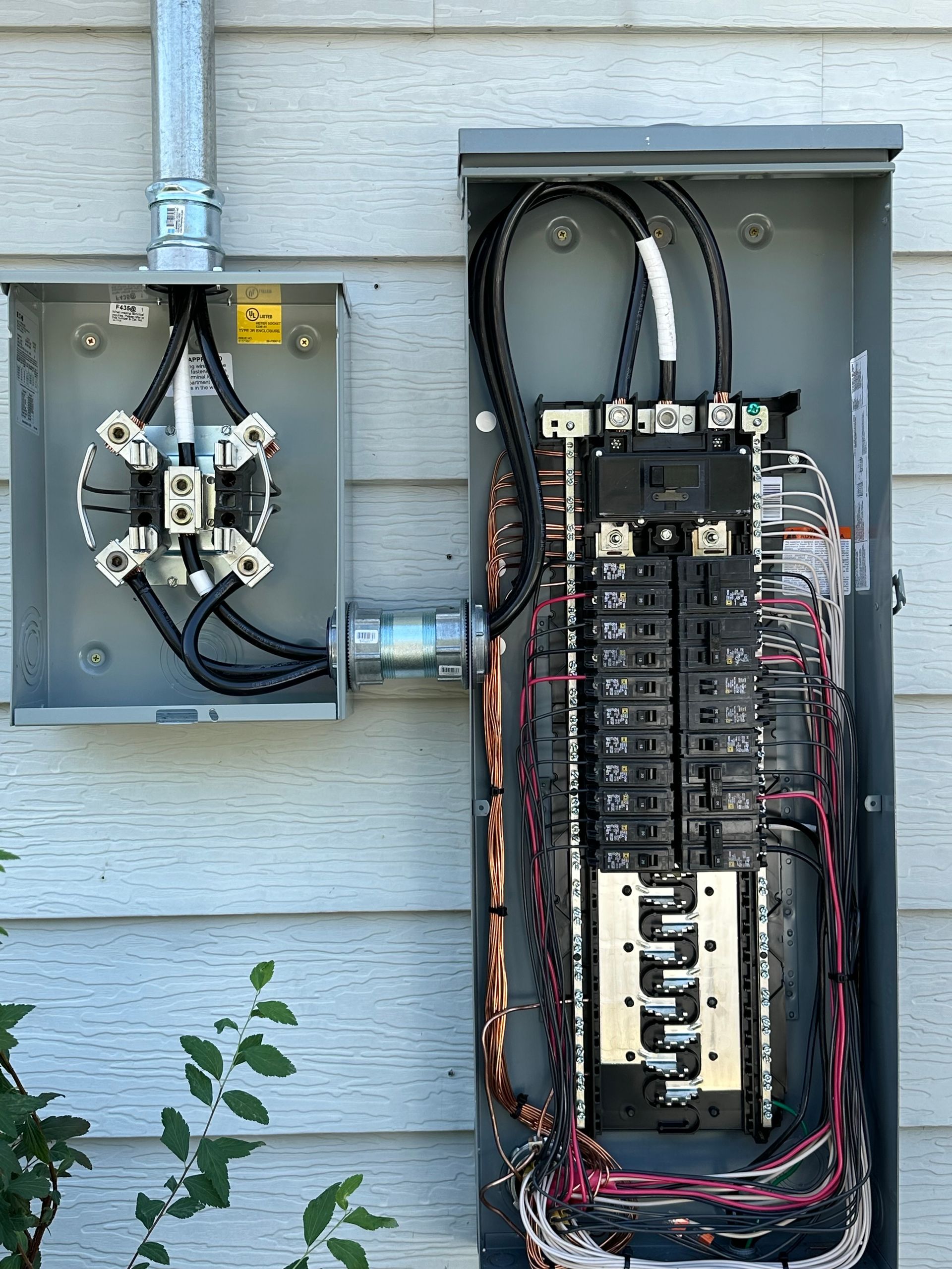 Open electrical panel and meter box on a gray siding wall. Wires and breakers are visible.