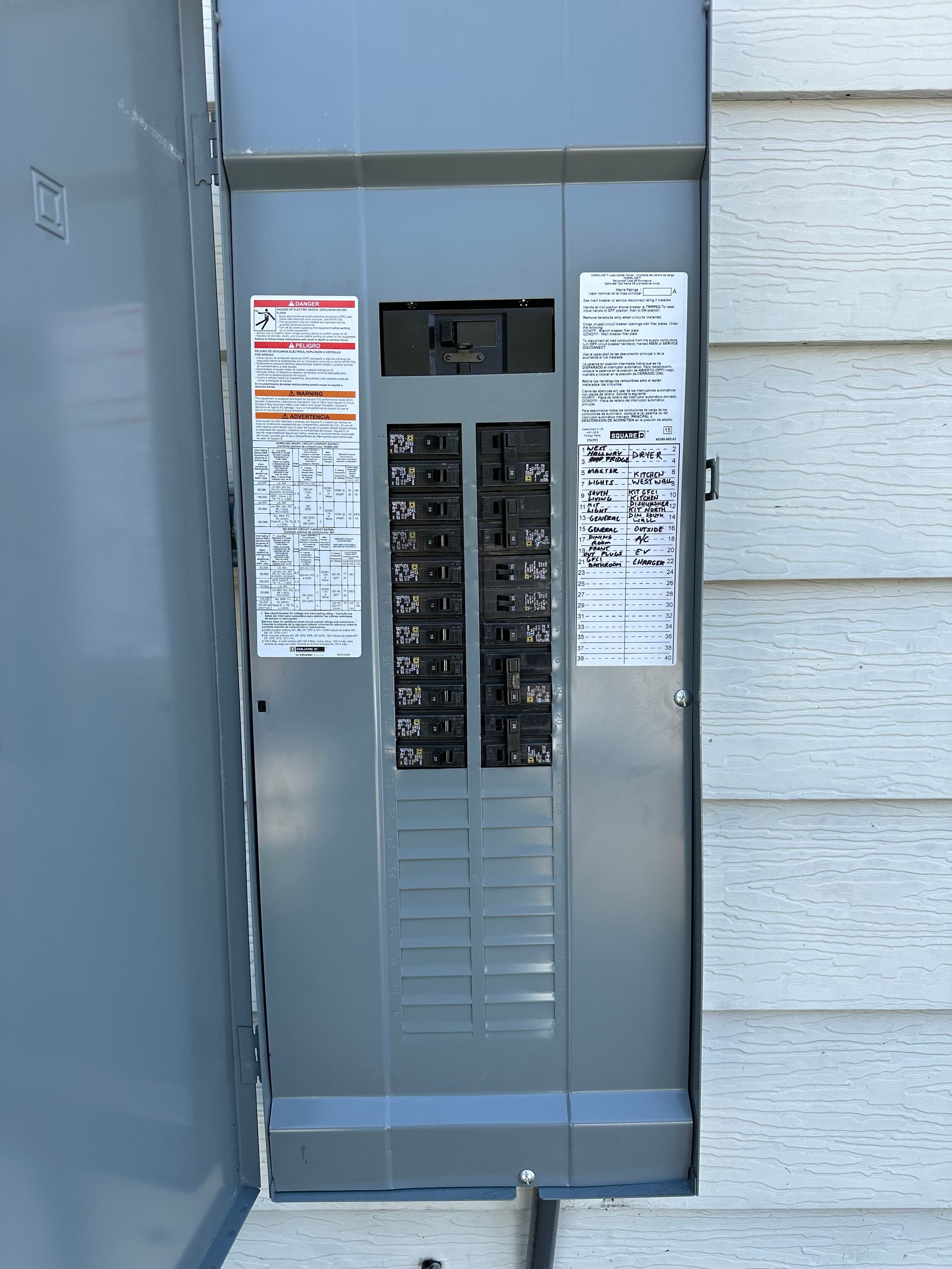Exterior electrical panel with multiple circuit breakers and labels, mounted on siding.
