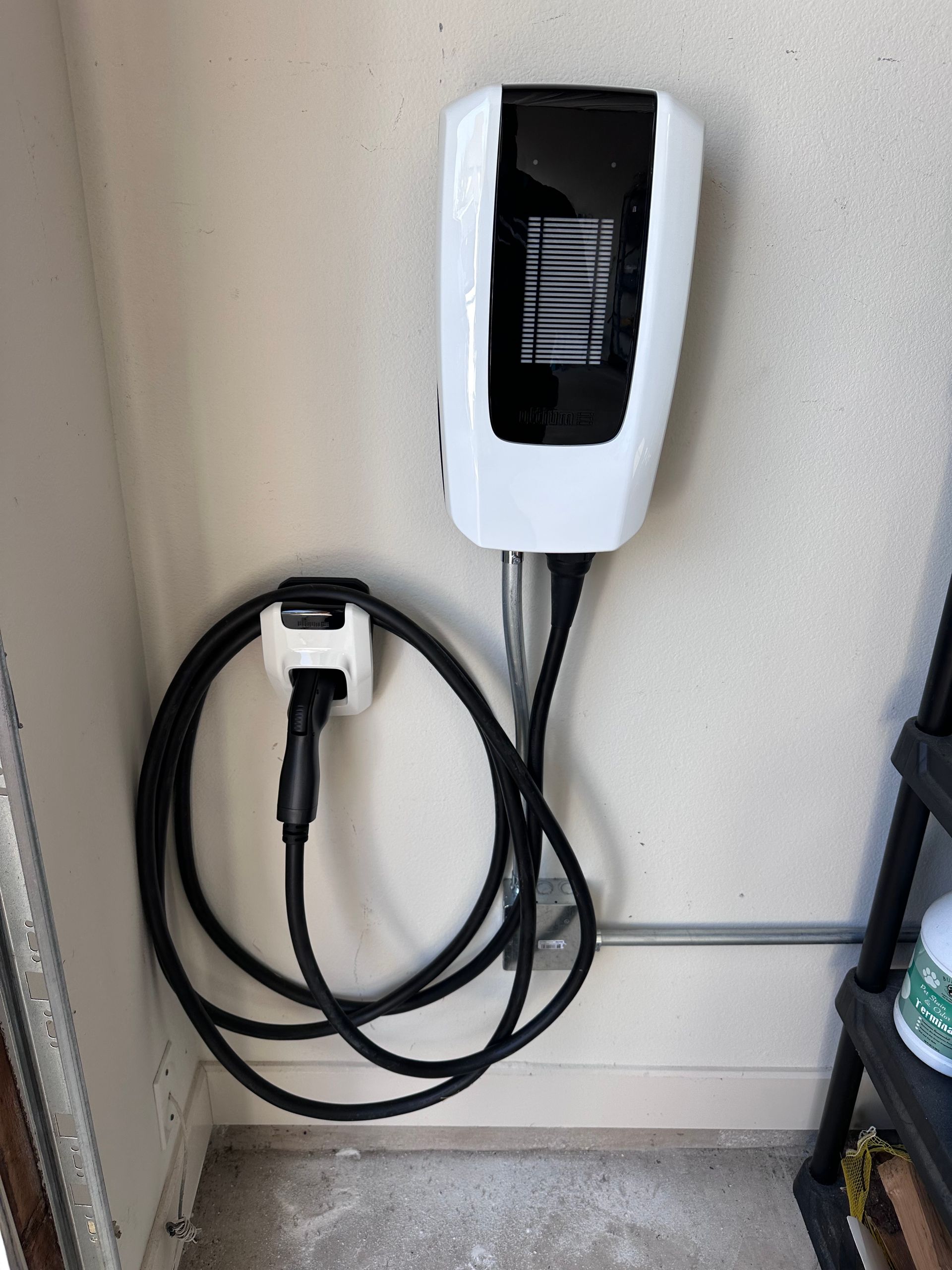 White electric vehicle charger mounted on a wall with black charging cable coiled below.