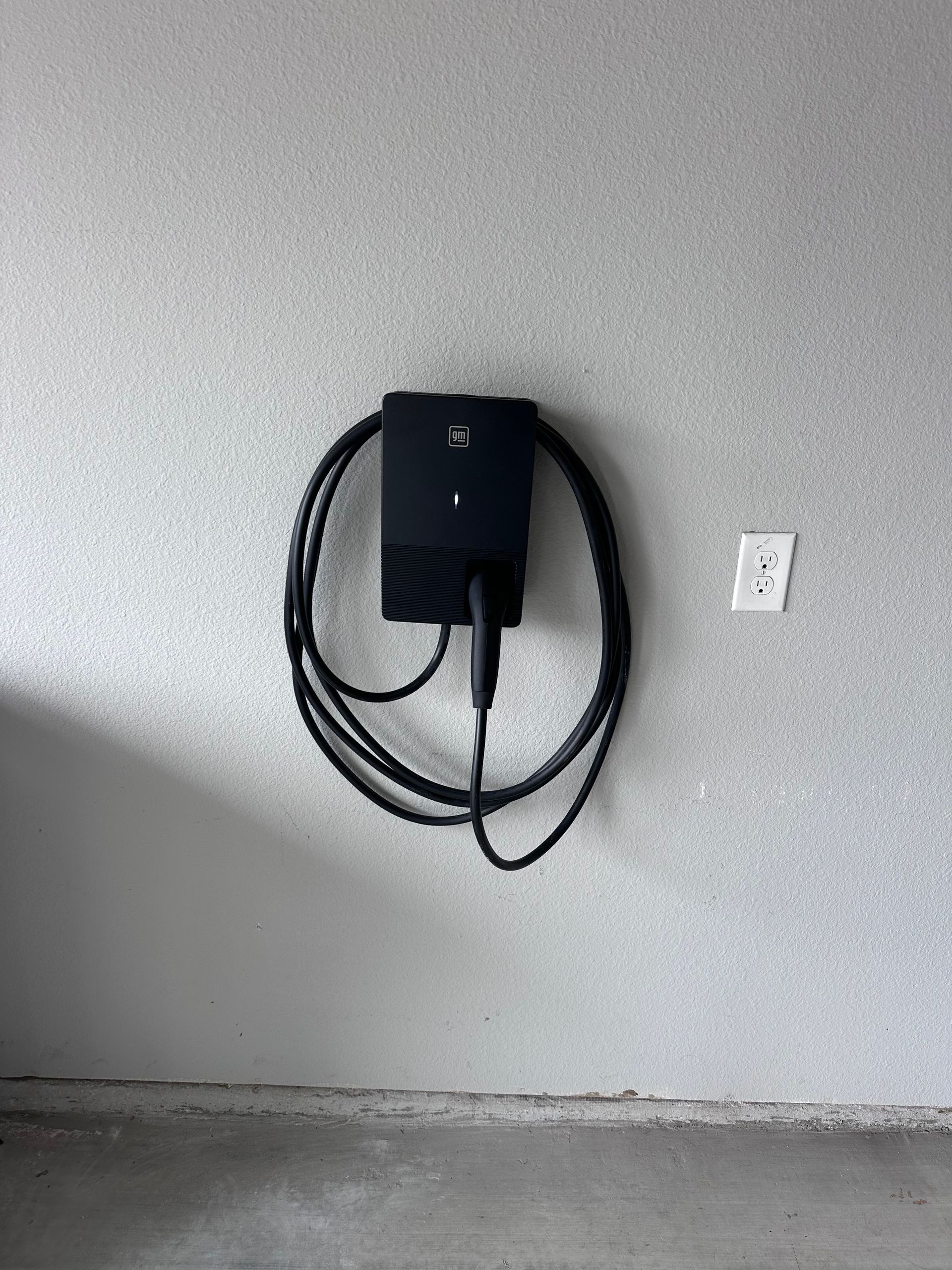 Black EV charger mounted on a textured, light gray wall, with the charging cable coiled.