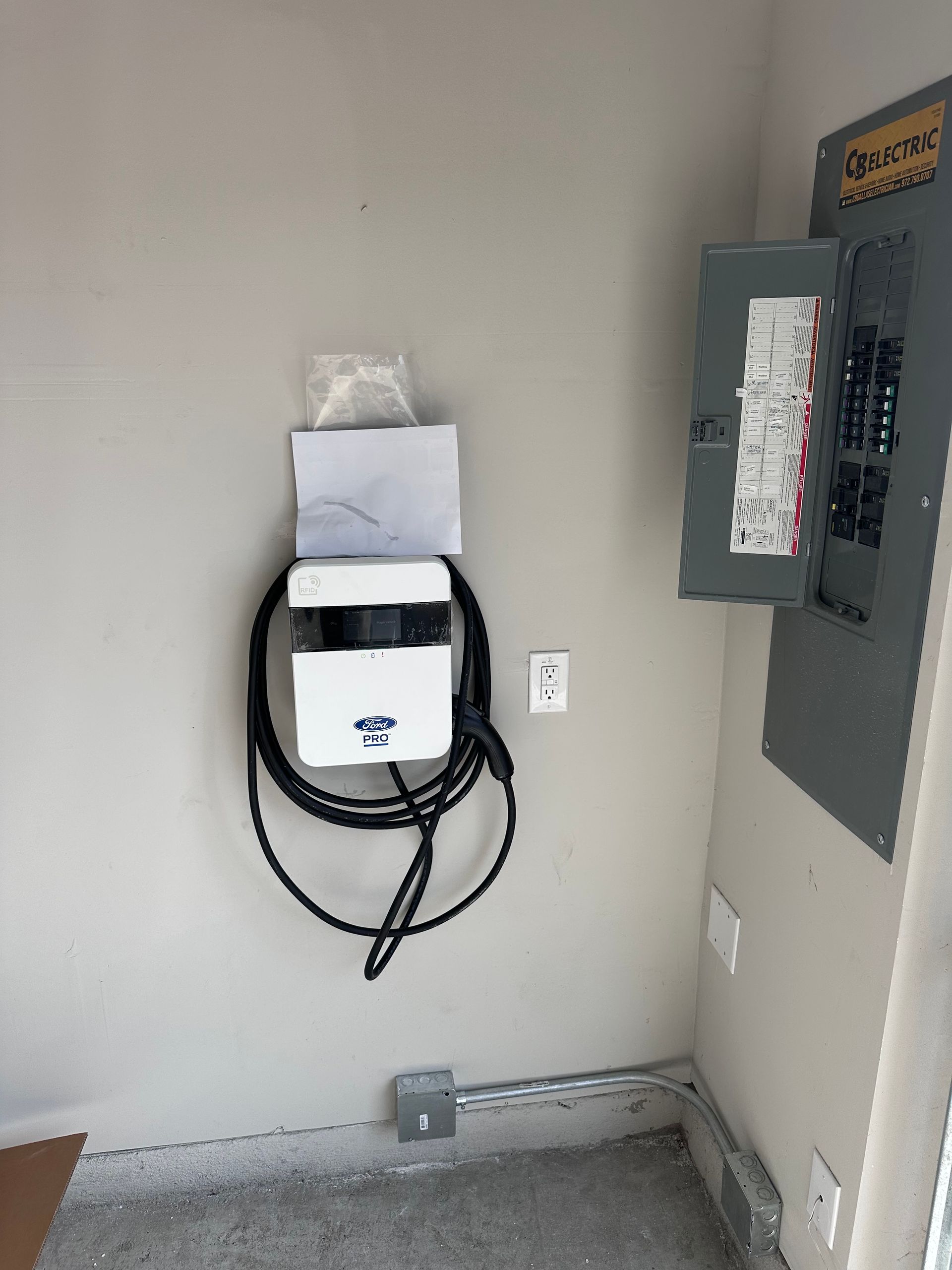 Electric vehicle charger and electrical panel mounted on a light gray wall in a garage.