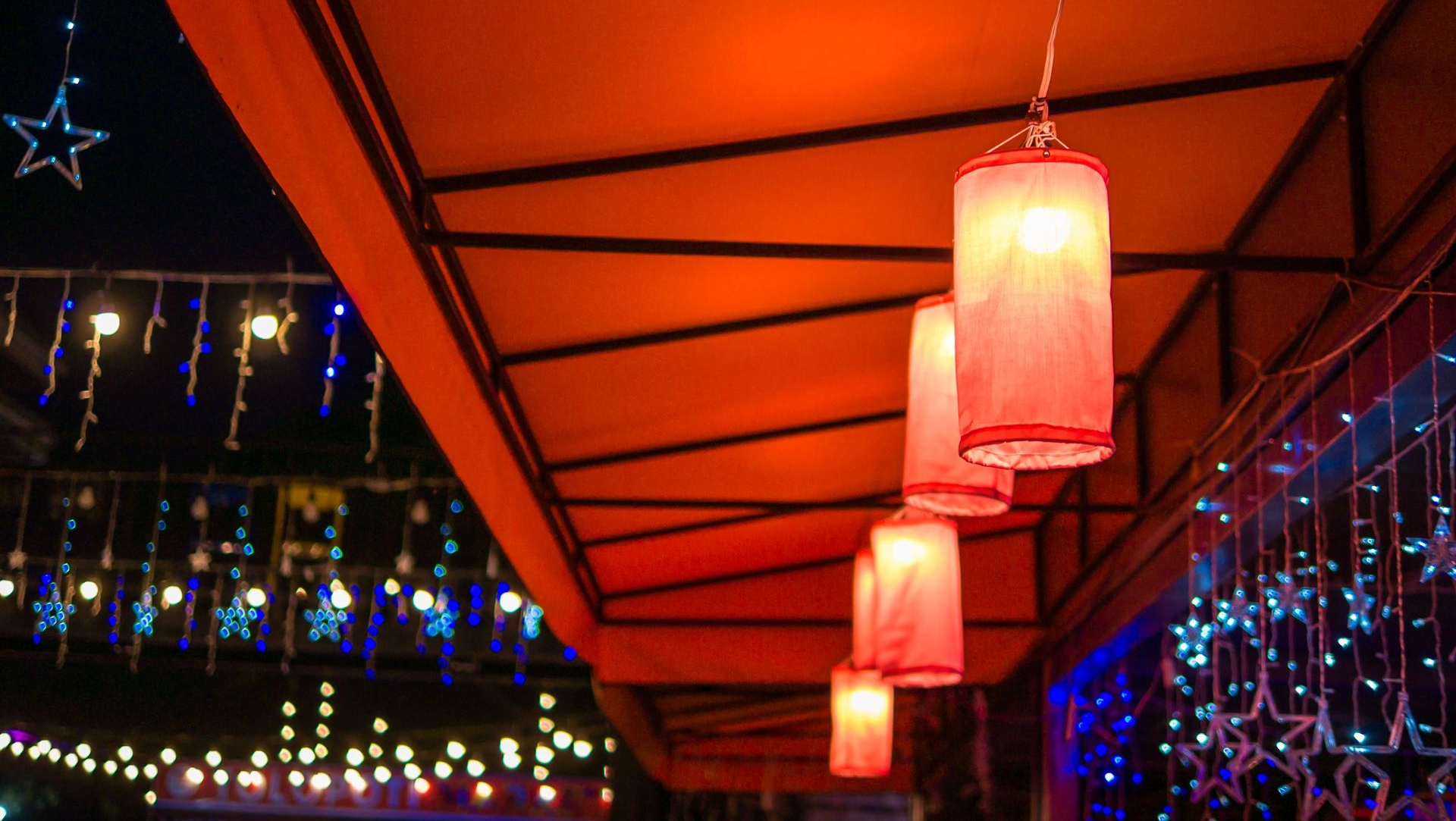 Red lanterns hang under an orange awning, strung with string lights at night.