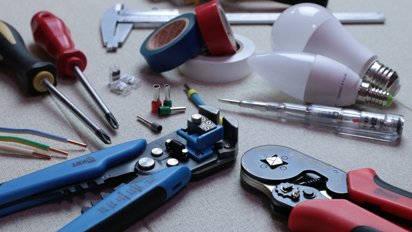 Electrical tools including screwdrivers, wire strippers, tape, and LED lightbulbs, on a white surface.