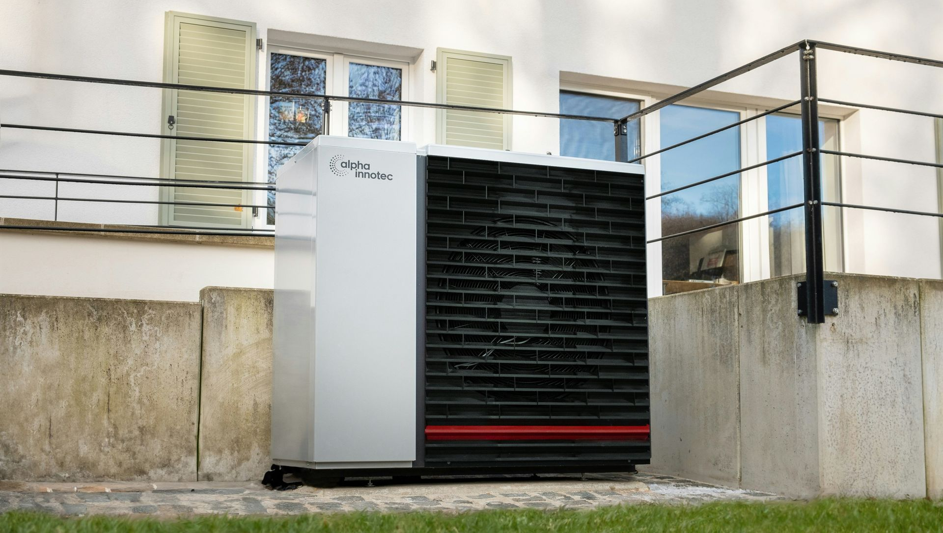 Outdoor heat pump unit next to a building, against a brick wall.