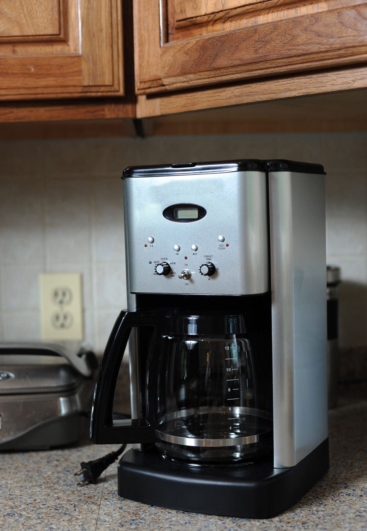 Silver coffee maker on a countertop in a kitchen; glass carafe visible.