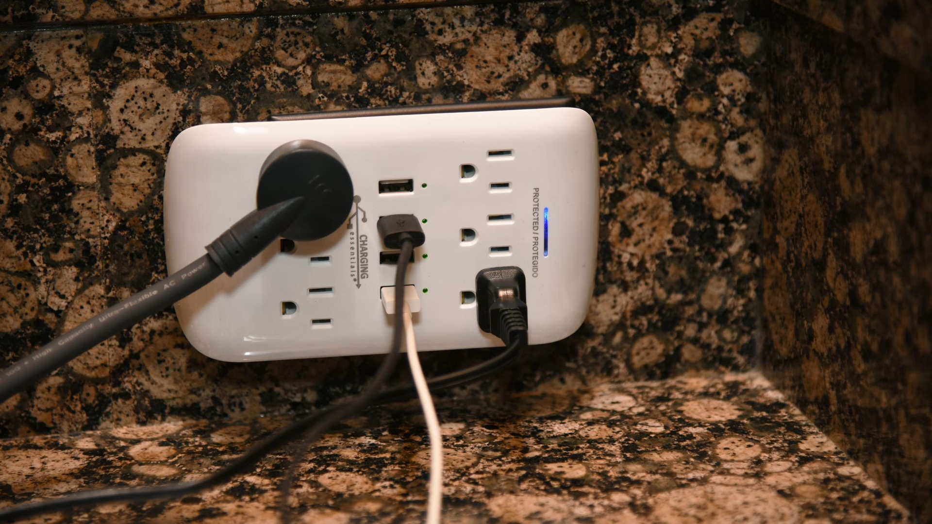 White power strip with multiple cords plugged into it, on a mottled brown surface.
