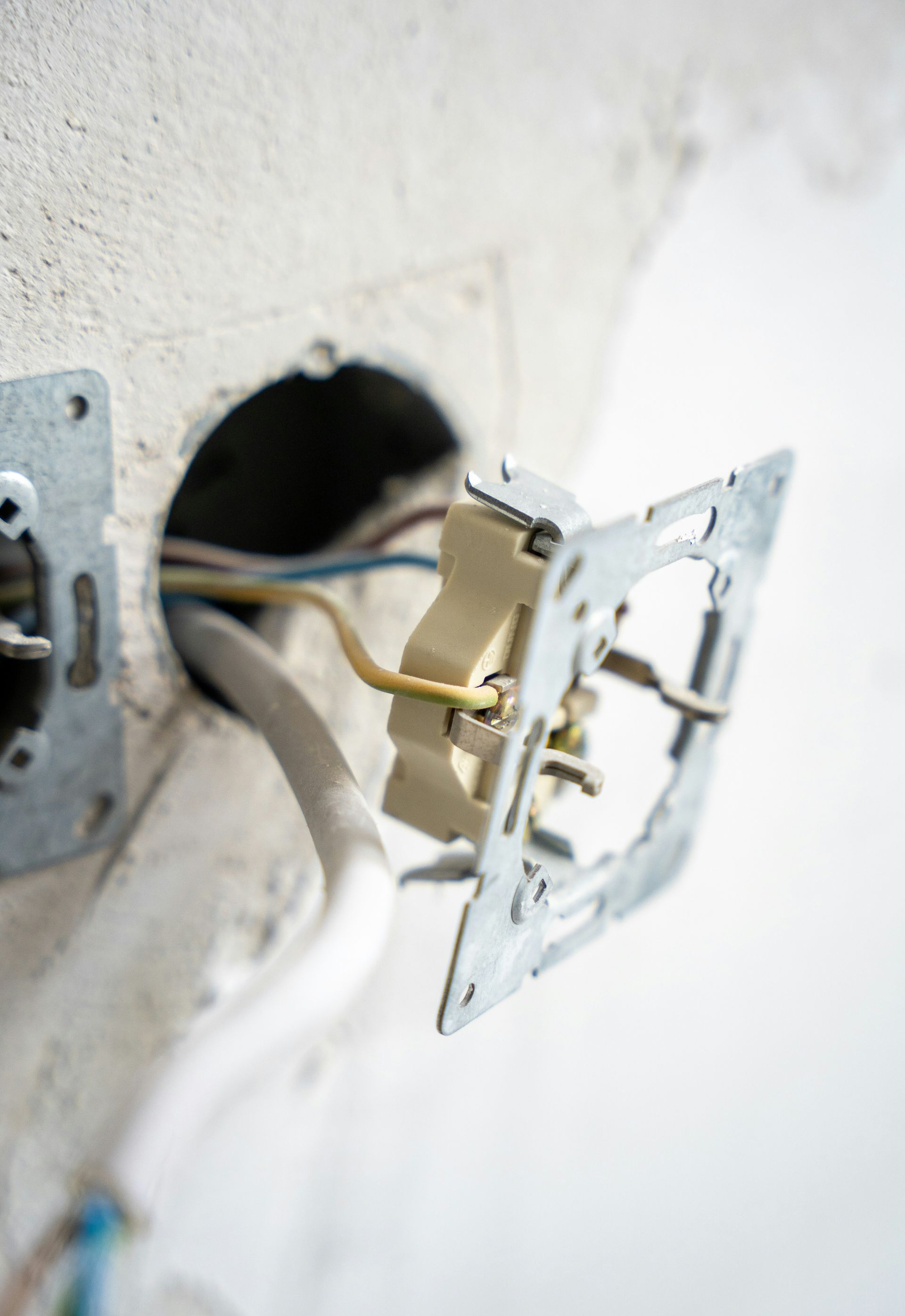 Electrical outlet with exposed wires and mounting plate in a wall.