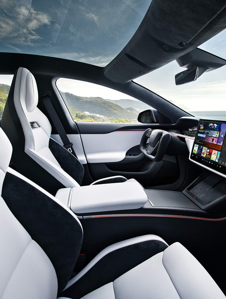 Interior view of a white and black Tesla with large touchscreen, sunny day, ocean visible.