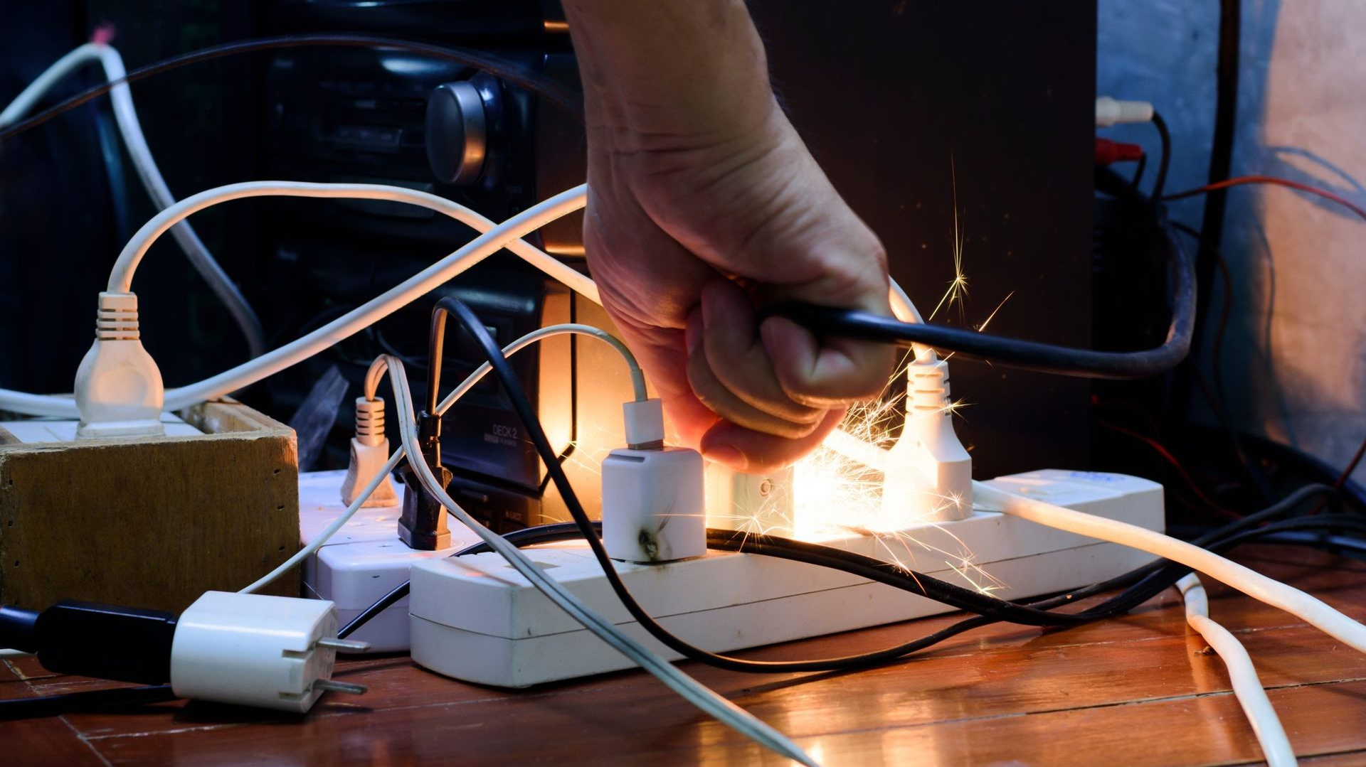 Hand touching electrical cord causing sparks near outlets and power strips.
