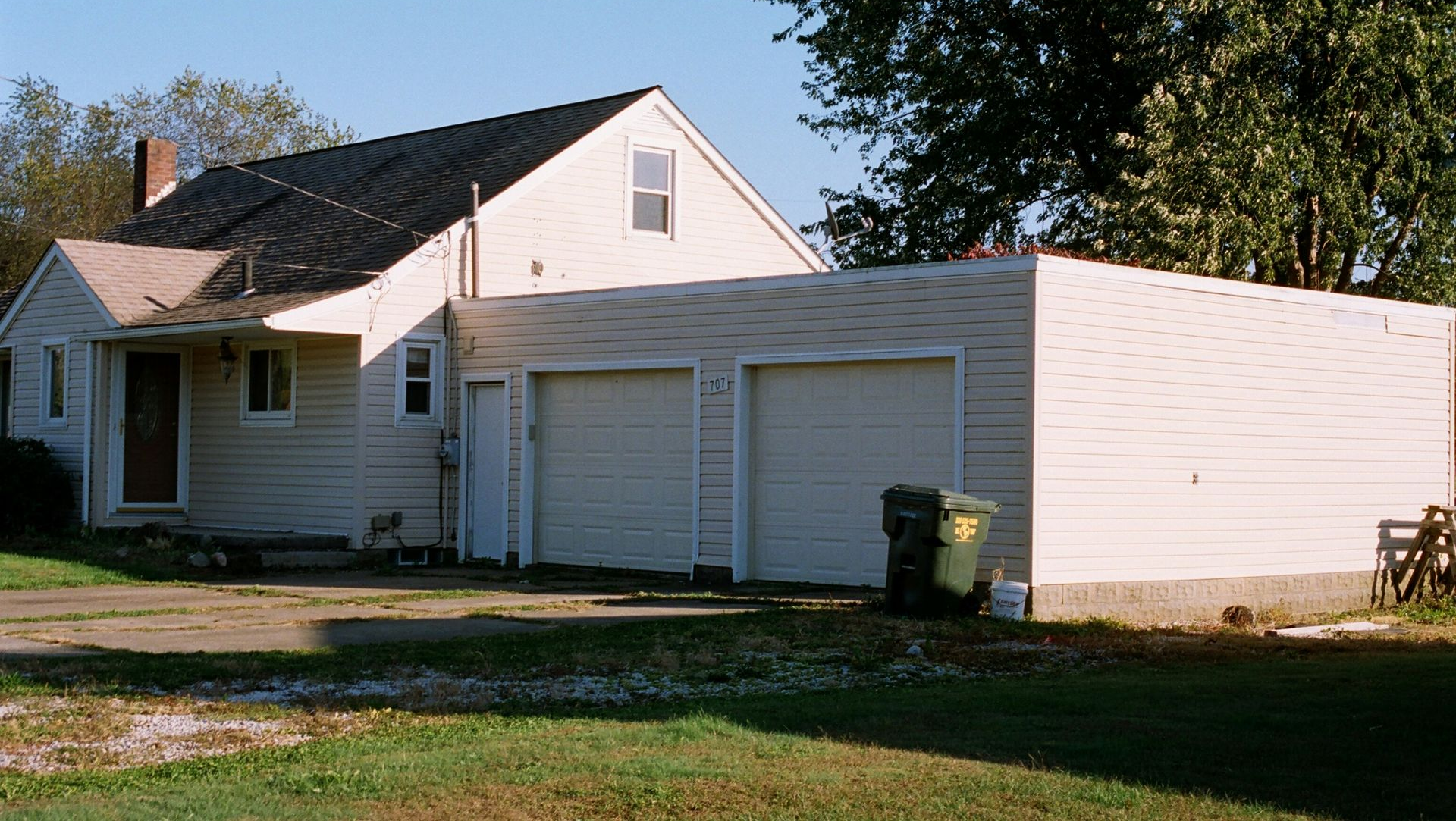Beige house with attached two-car garage, driveway, and green lawn under a blue sky.