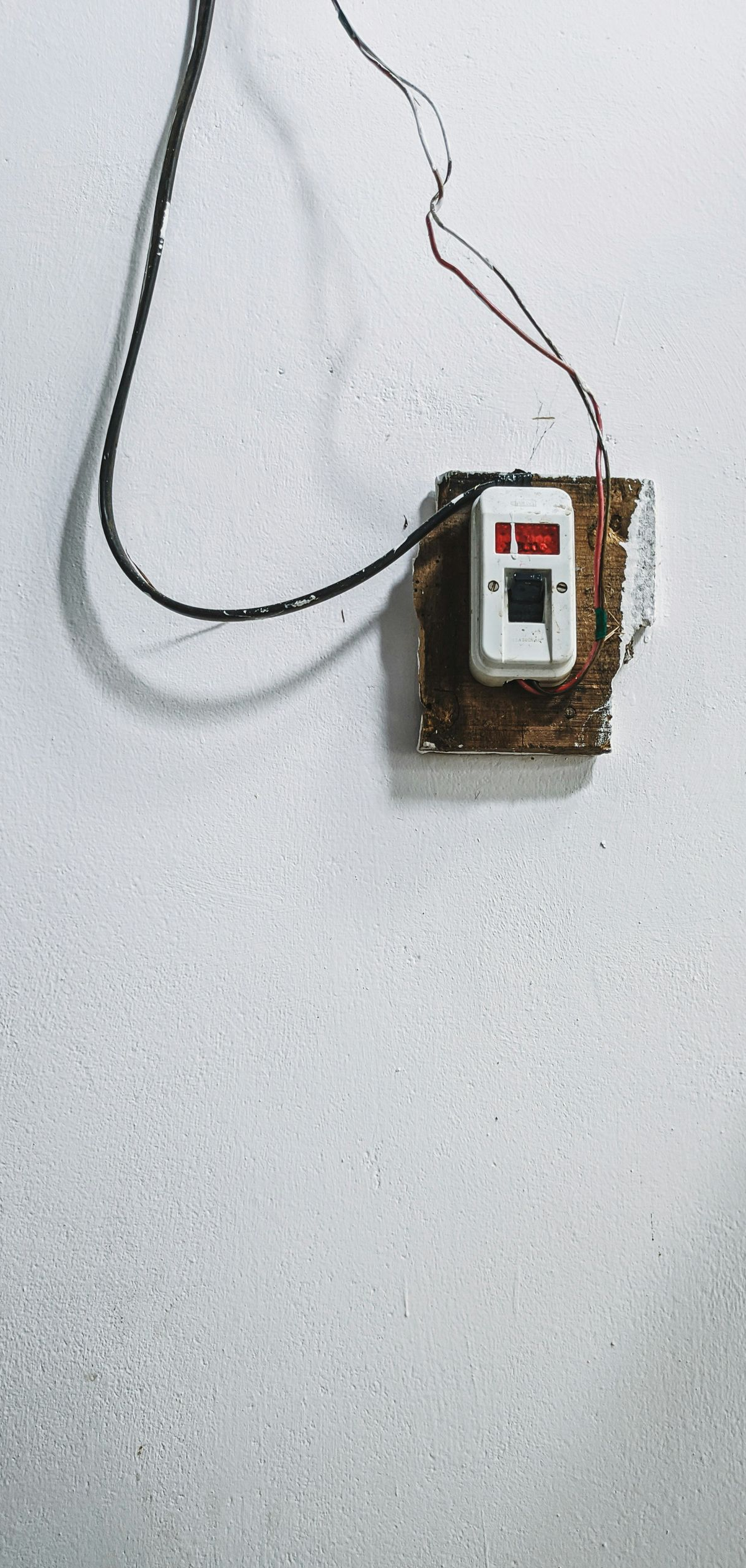 Damaged electrical switch on a white textured wall with exposed wires.