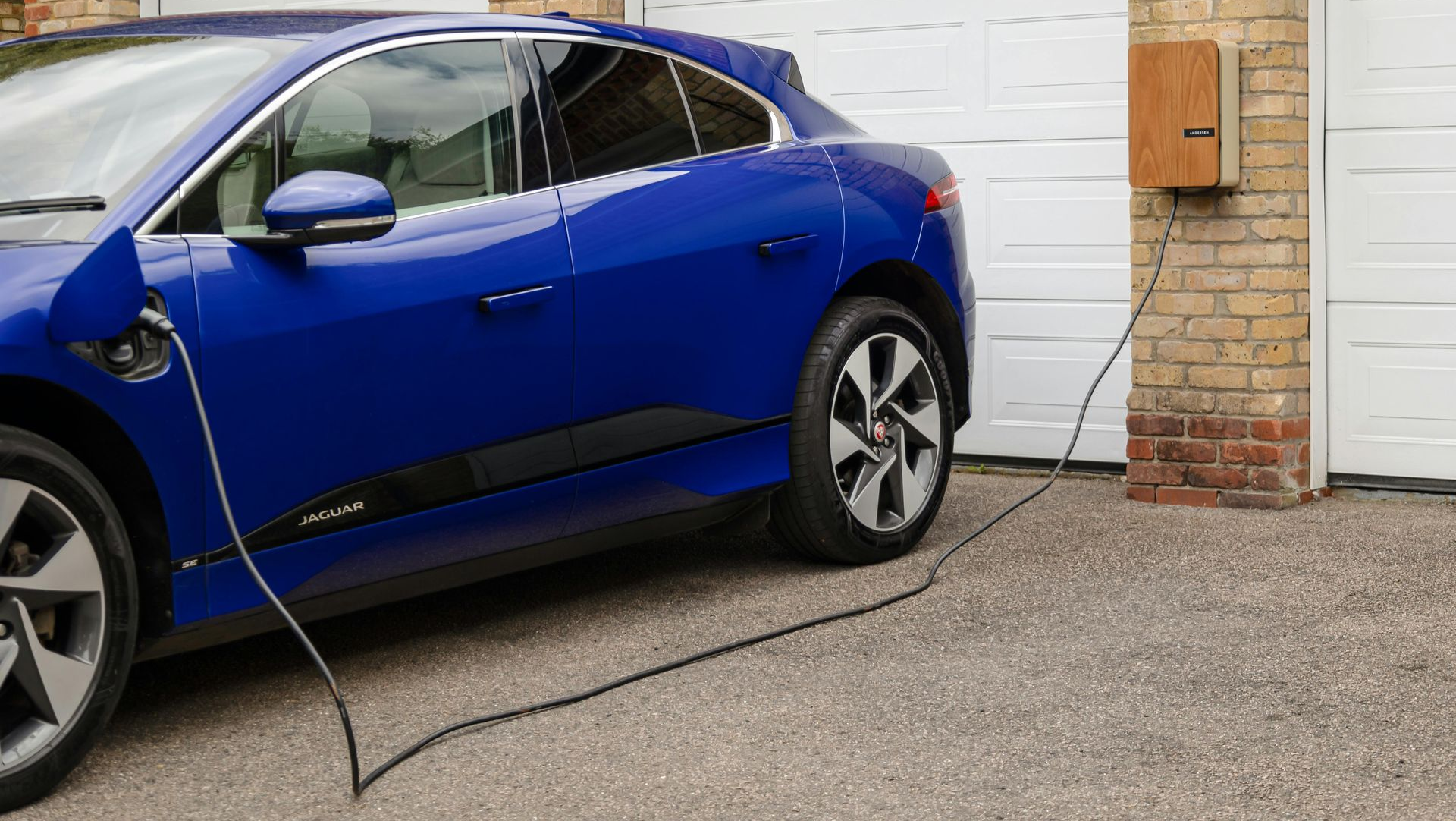 Blue electric car charging at a home garage with a charger box on the wall.