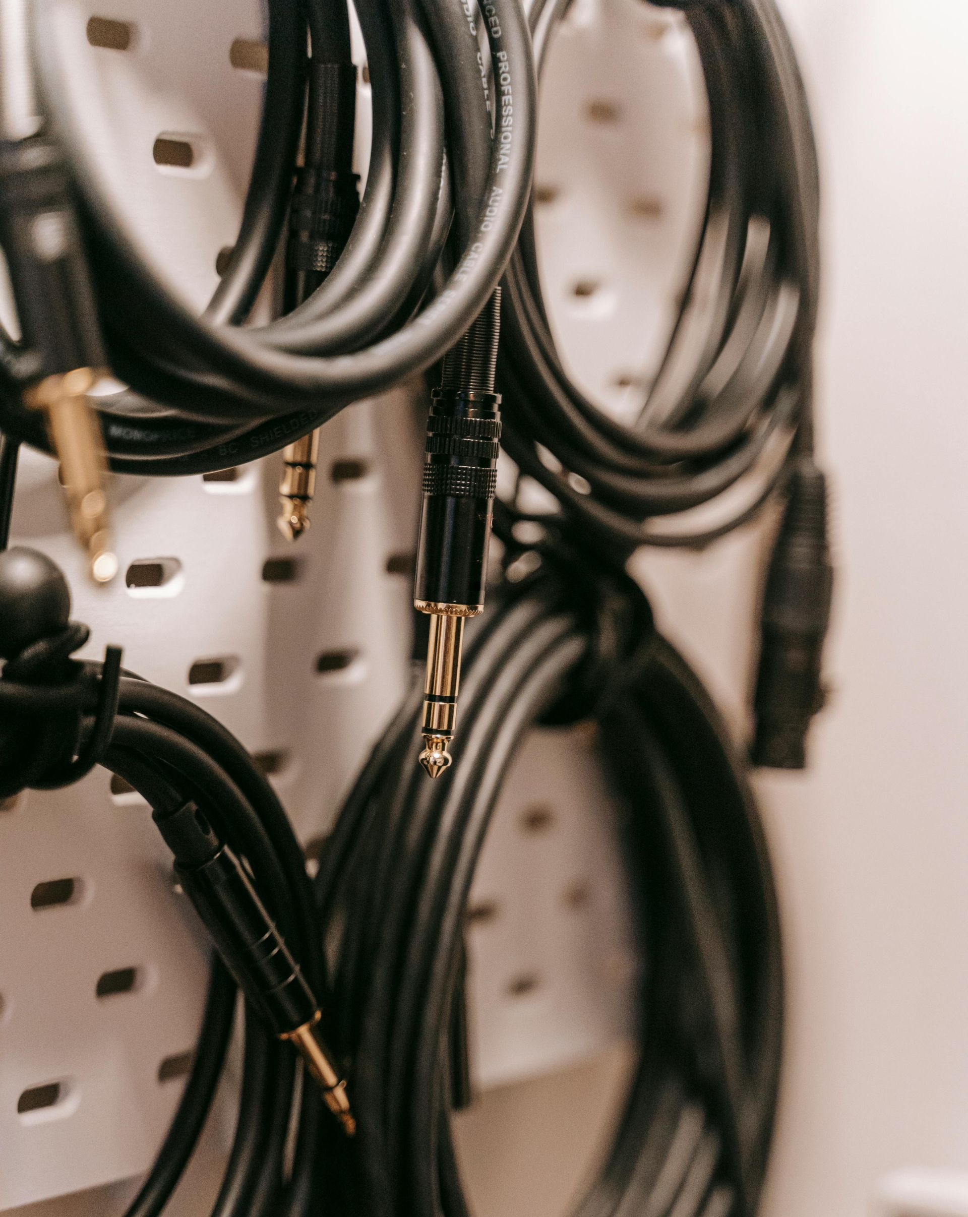 Black audio cables hanging on a white pegboard, showing various connector types.