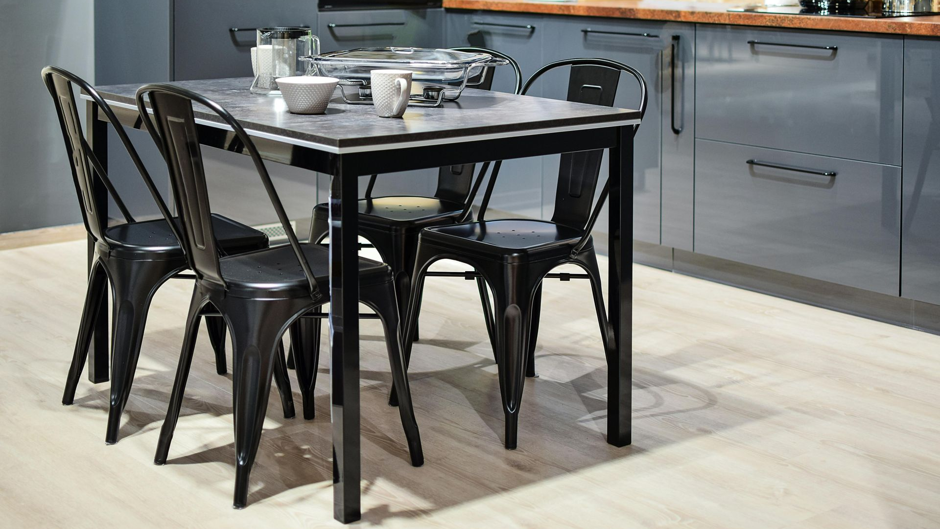 A dining table with four black metal chairs in a modern kitchen with gray cabinets and wood countertop.