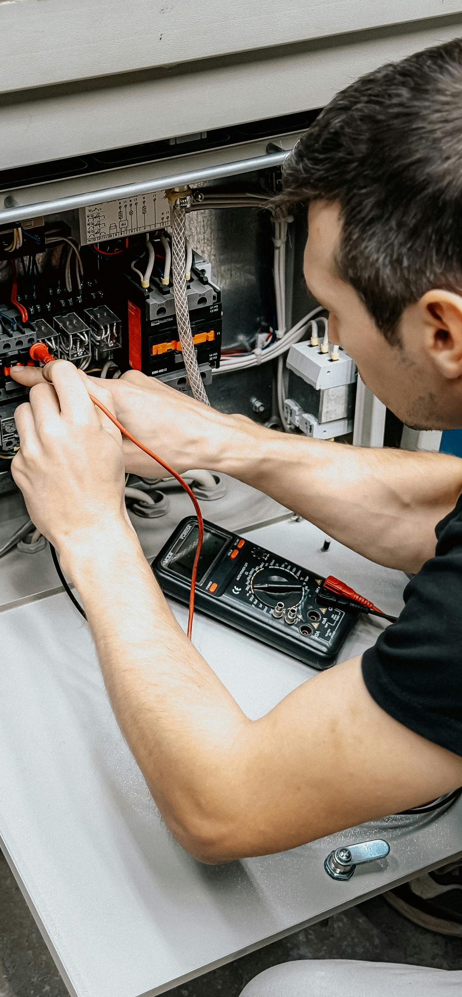 A person tests electronics with a multimeter. They are working inside a metal cabinet, focusing intently.
