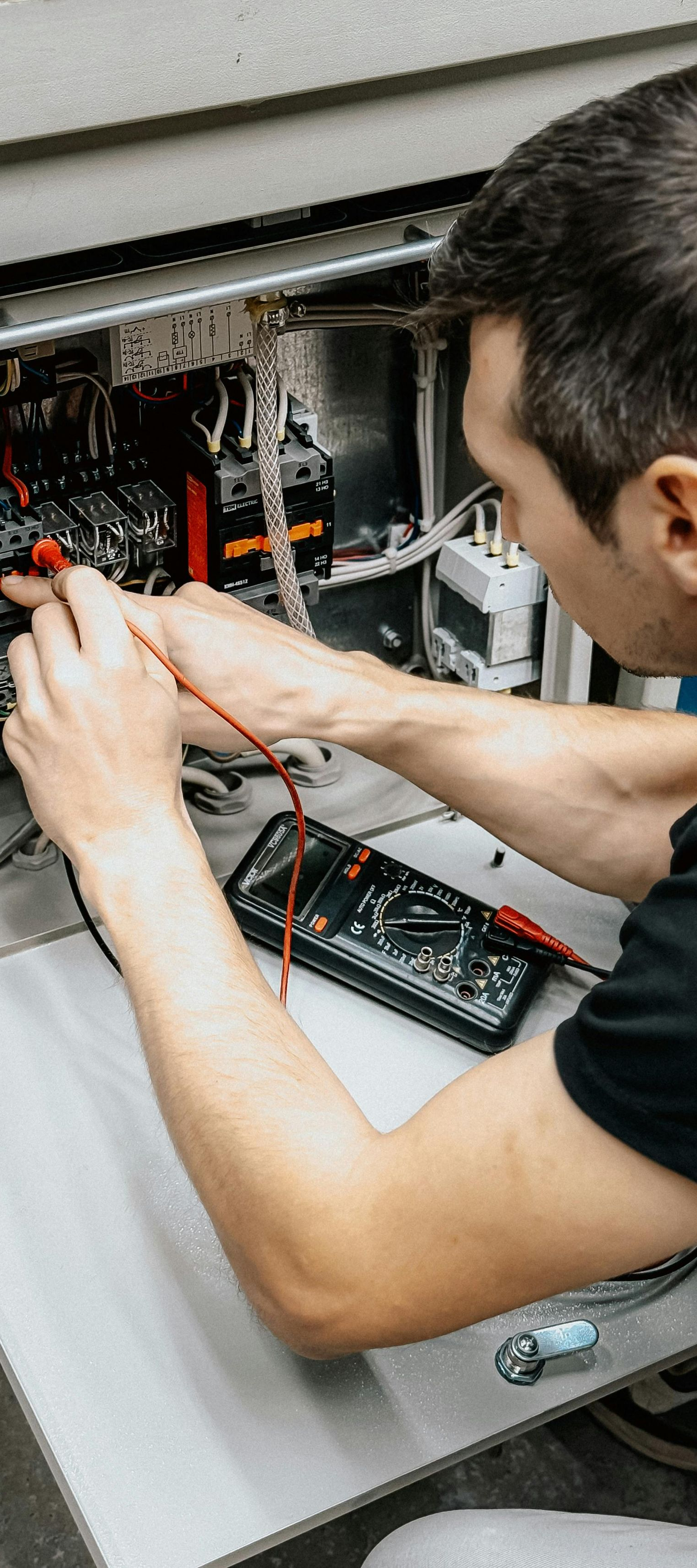 A person using a multimeter to test electrical components inside of a machine.