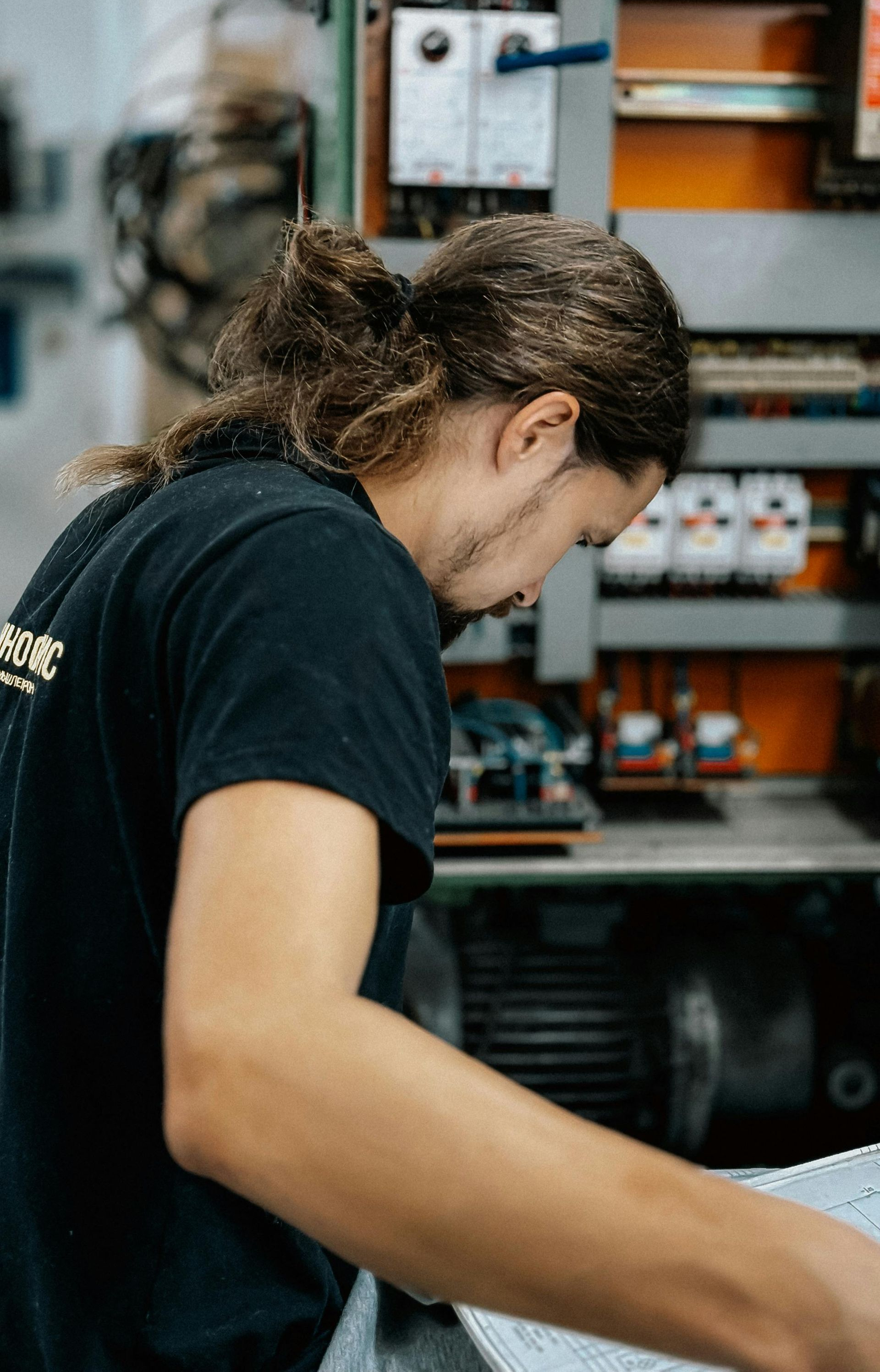 Person with long hair in a bun working on machinery, looking down at a paper.