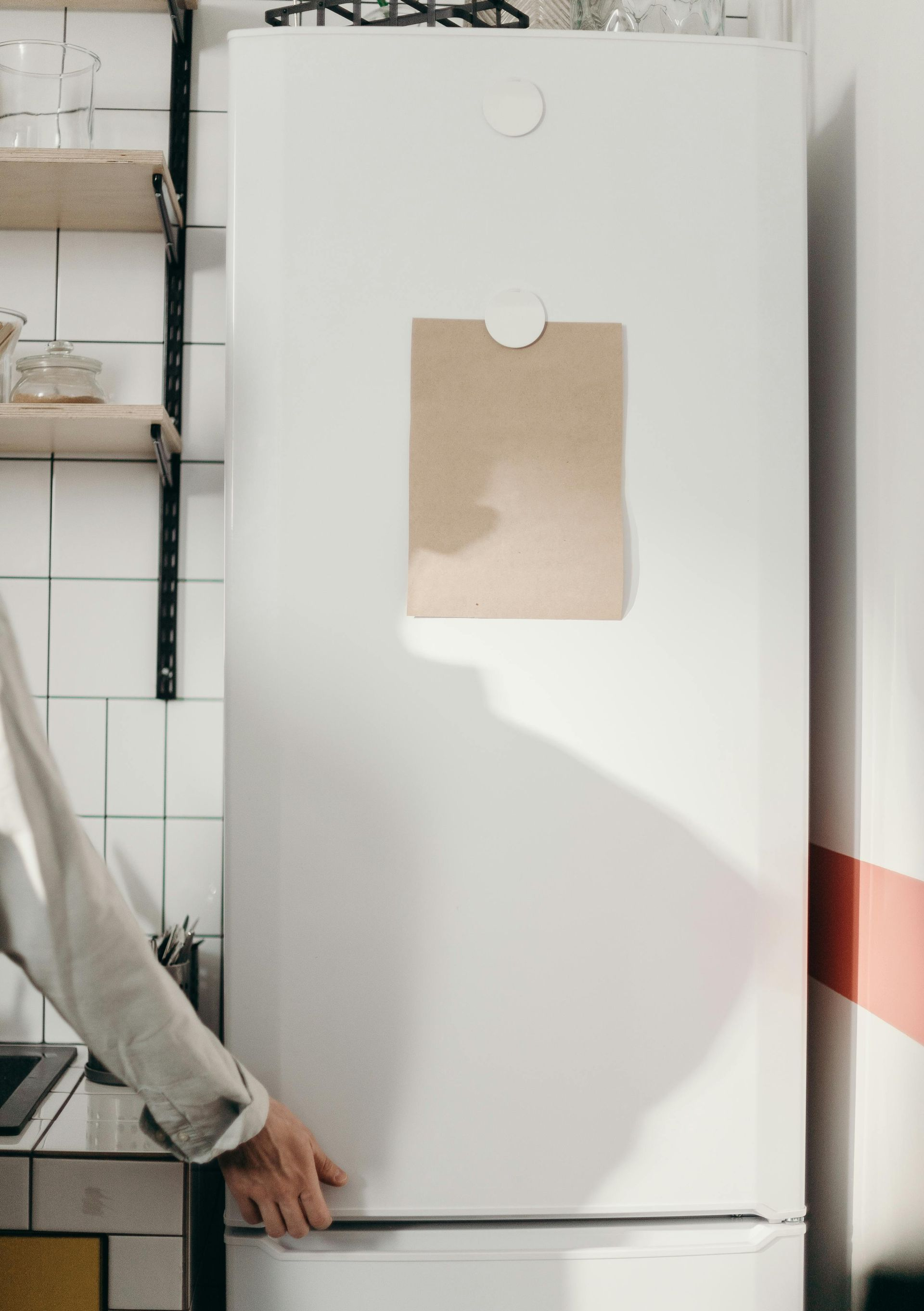 White refrigerator with brown paper bag on the door, person opening the door, kitchen setting.
