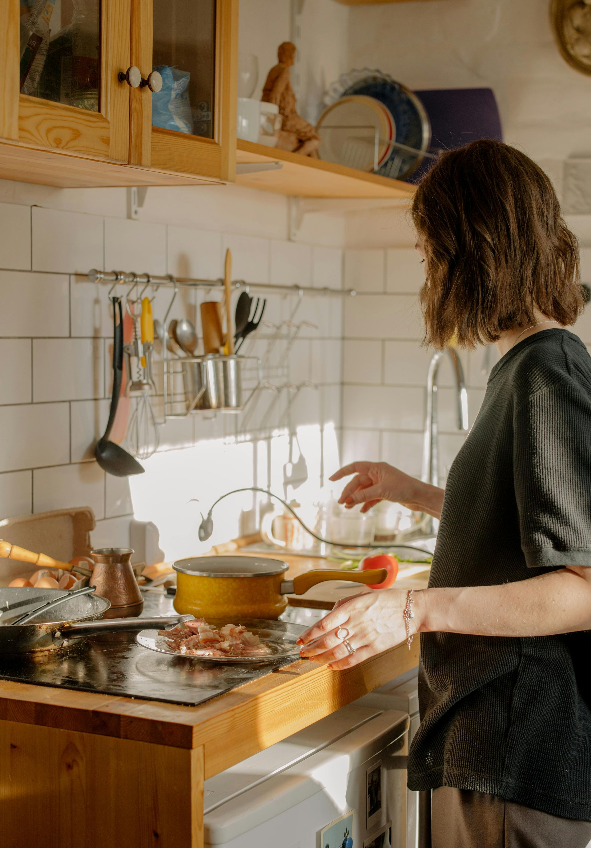 Woman cooking in kitchen, reaching for something on countertop. Sunlight streams in.