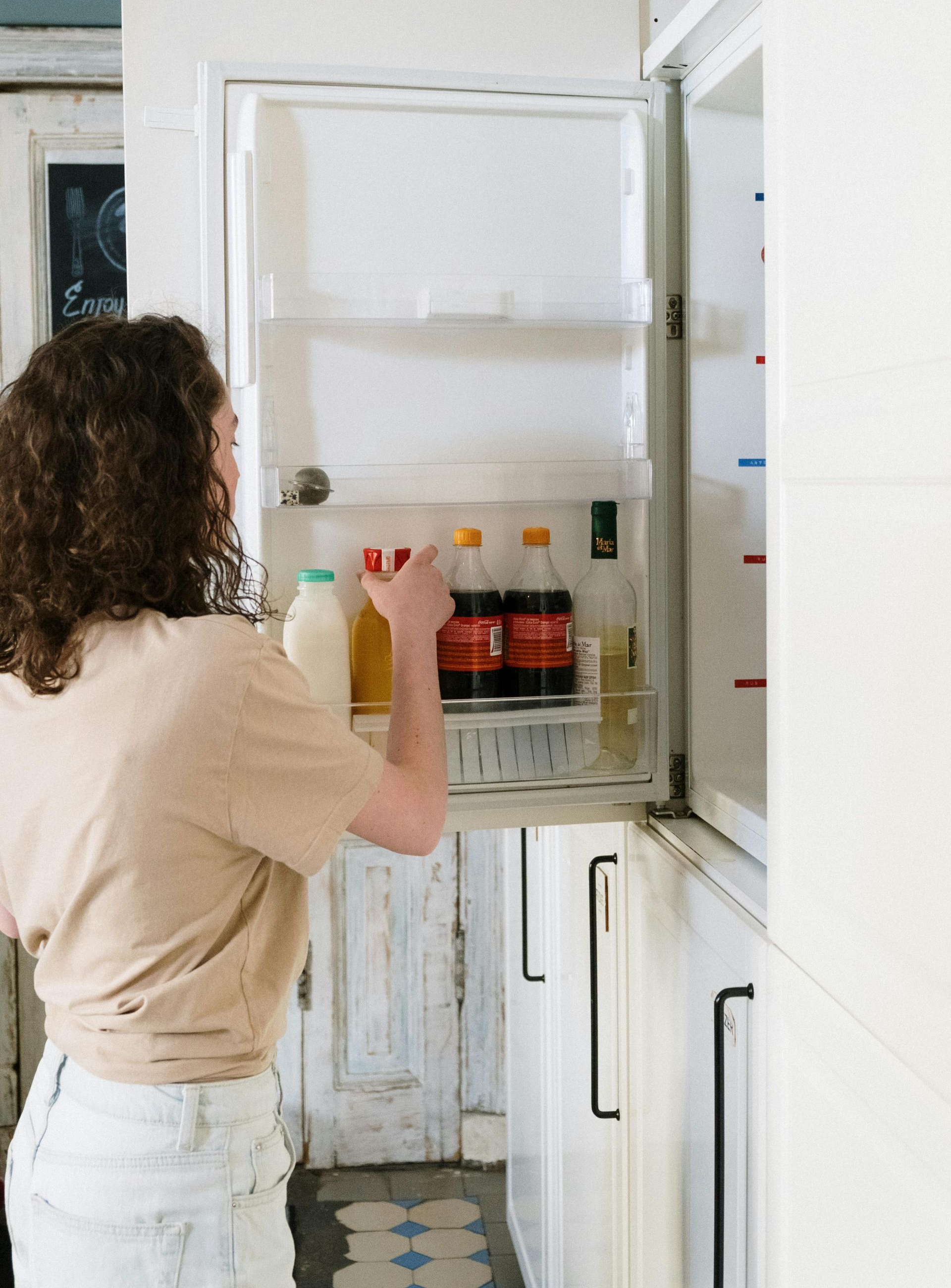 Woman reaching into open refrigerator in a white kitchen.