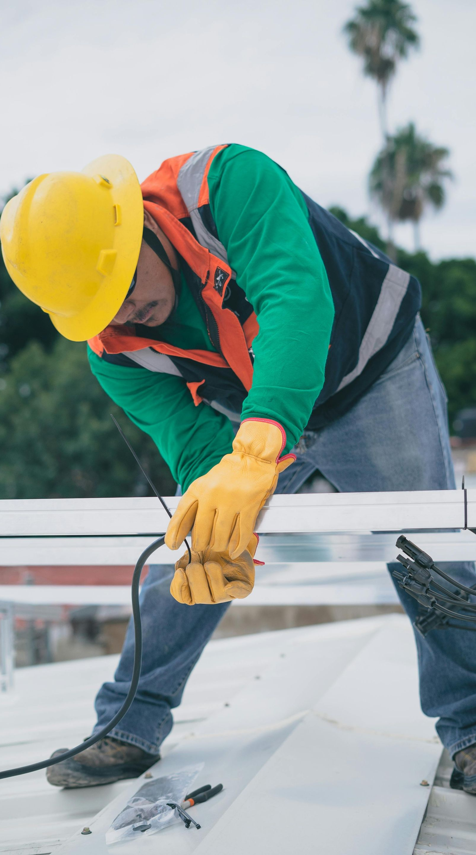 Person in safety gear working on a roof, using a tool.