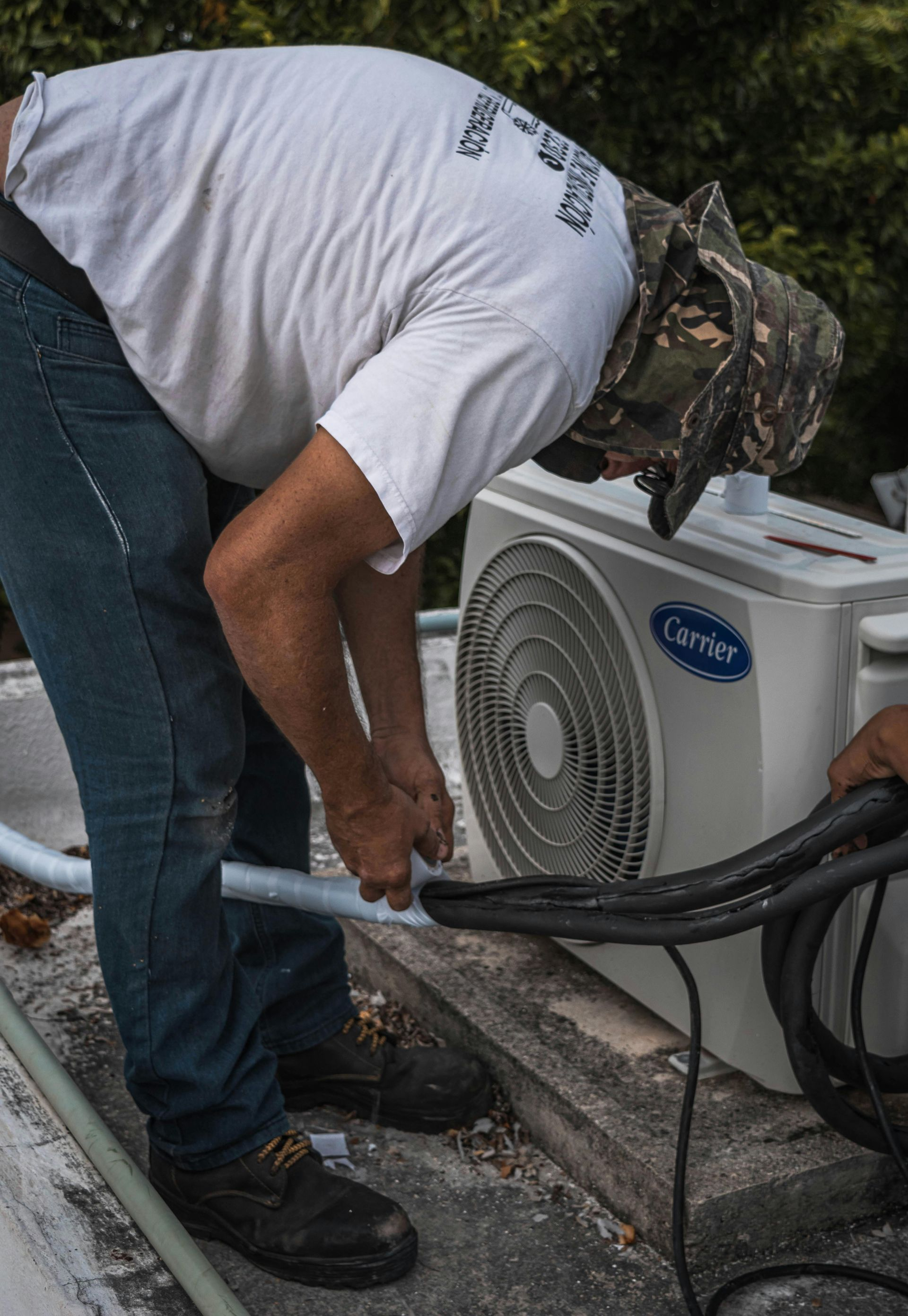 Man in white shirt and hat working on an outdoor air conditioning unit on a rooftop.