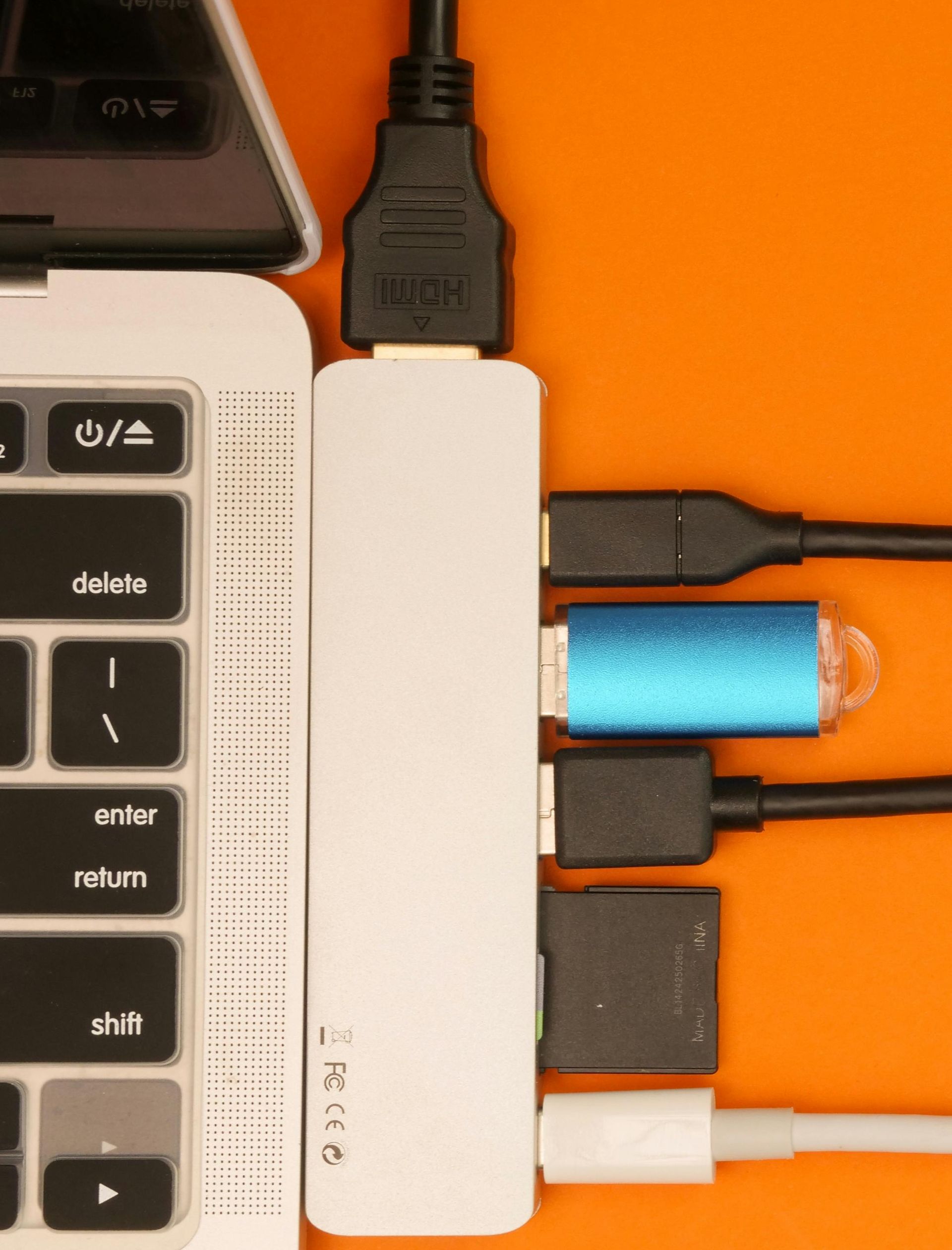 Laptop connected to a white USB hub with multiple cables plugged in; orange background.