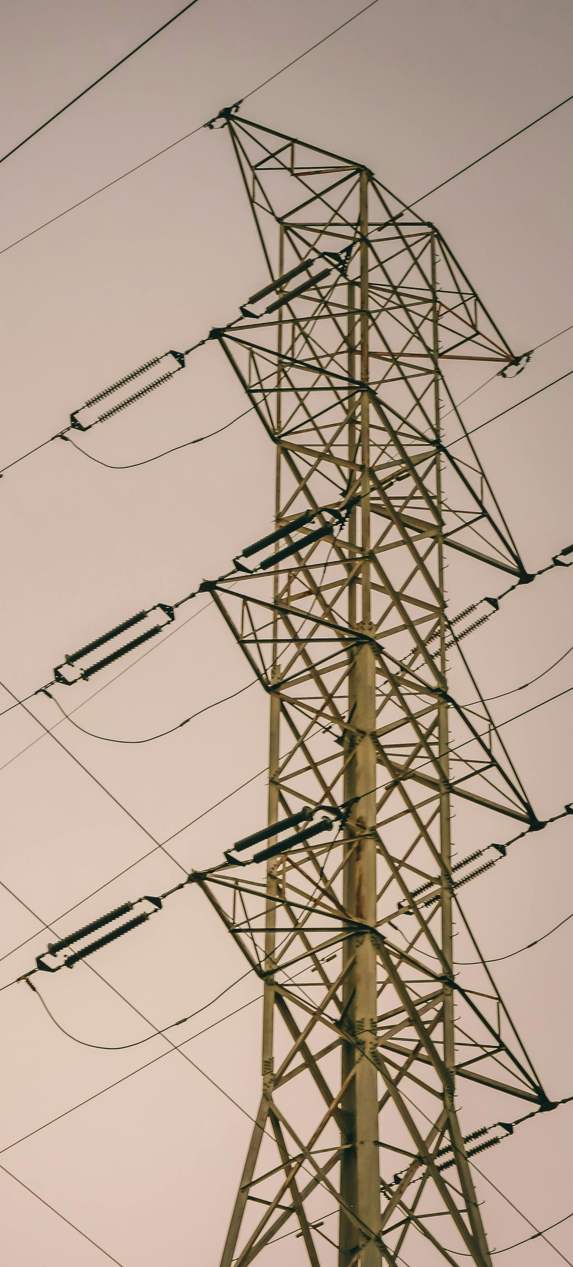 A tall electricity pylon against a pale sky, power lines extending outwards.