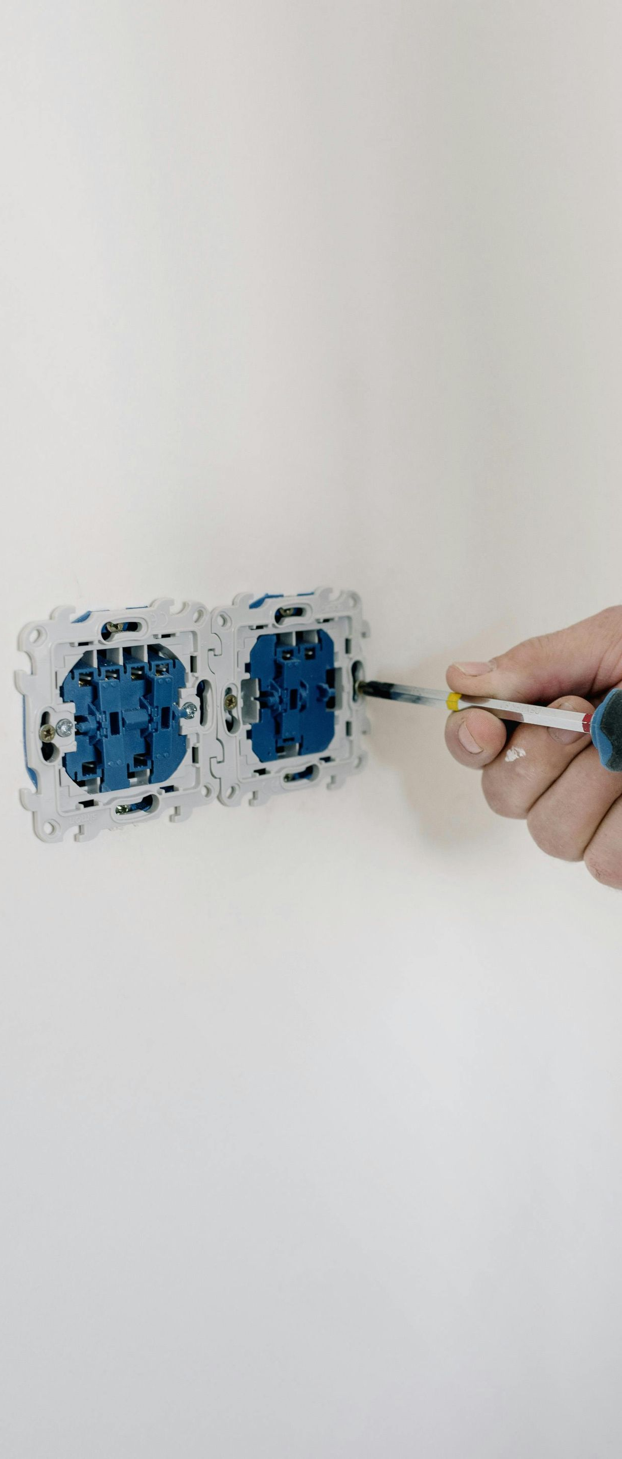 Person installing an electrical outlet with a screwdriver on a white wall.