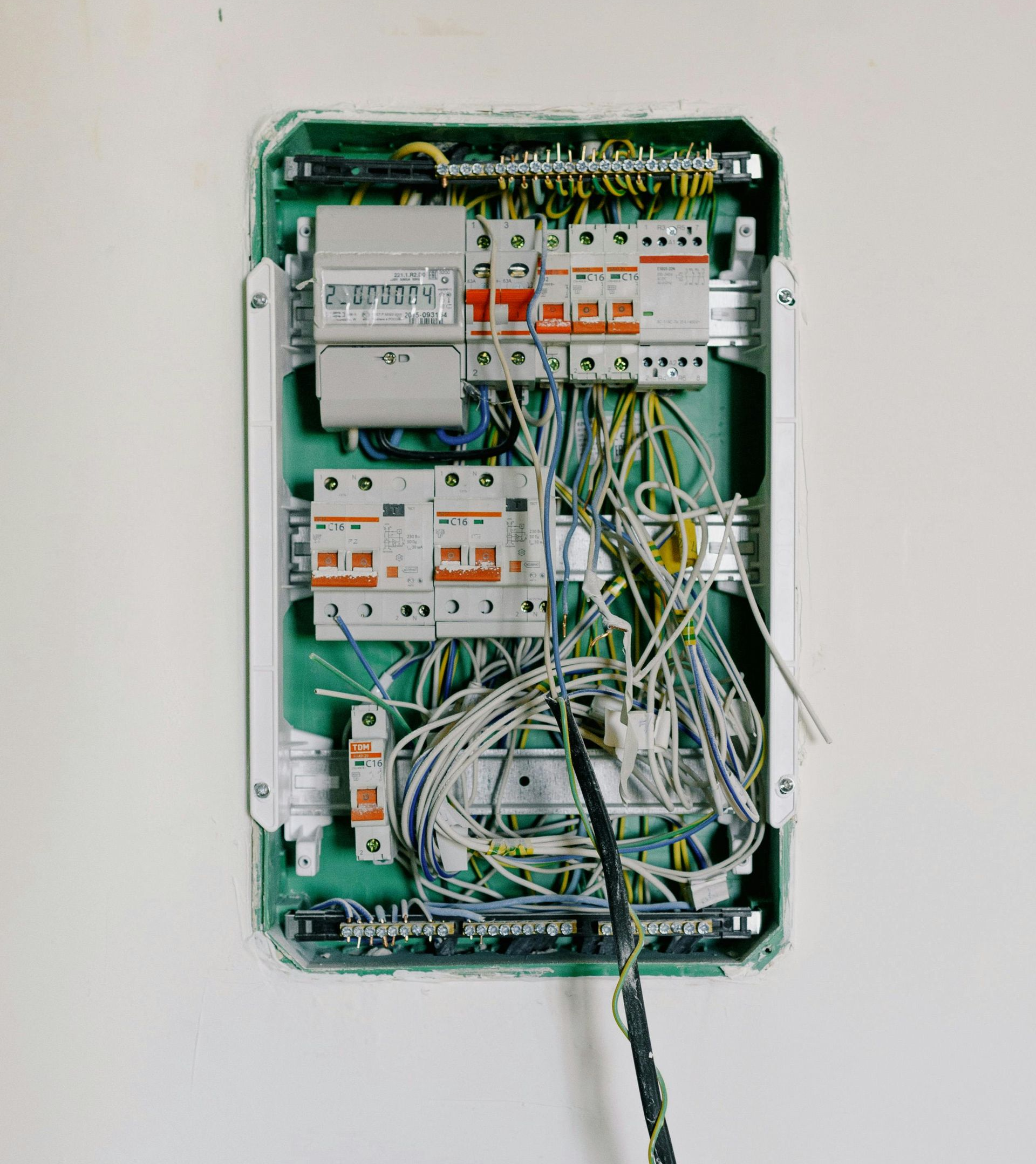 Open electrical panel with multicolored wires in a white wall.