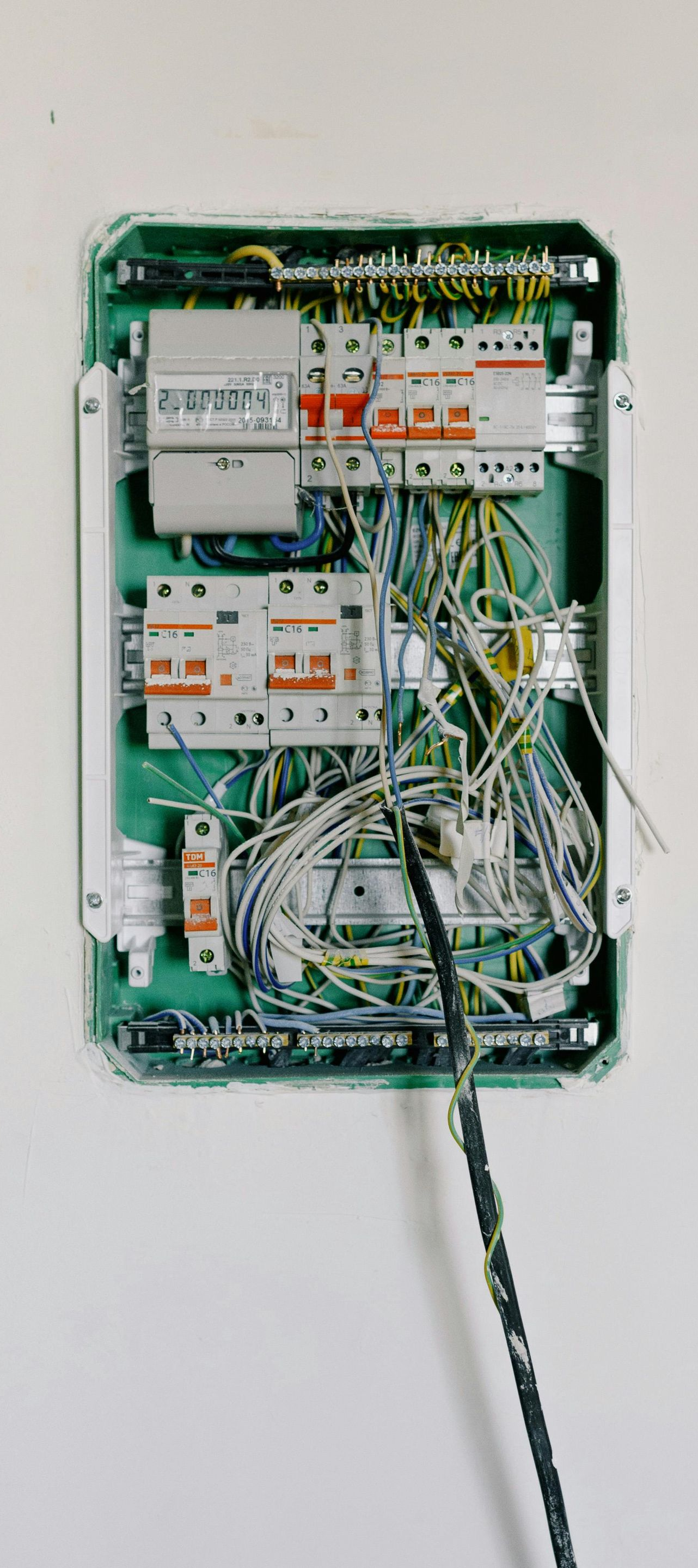 Electrical panel with exposed wires and breakers, mounted on a white wall.