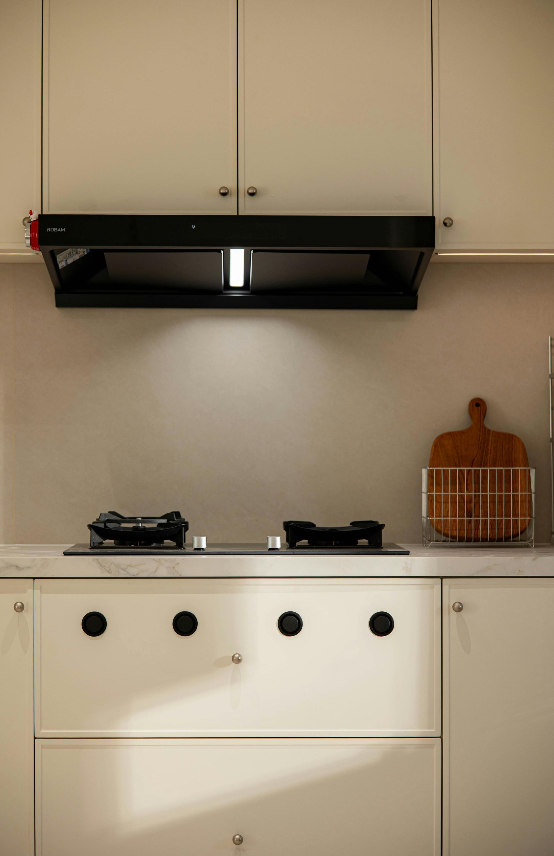 White kitchen with stovetop, range hood, and cabinets. A wooden cutting board sits on the counter.