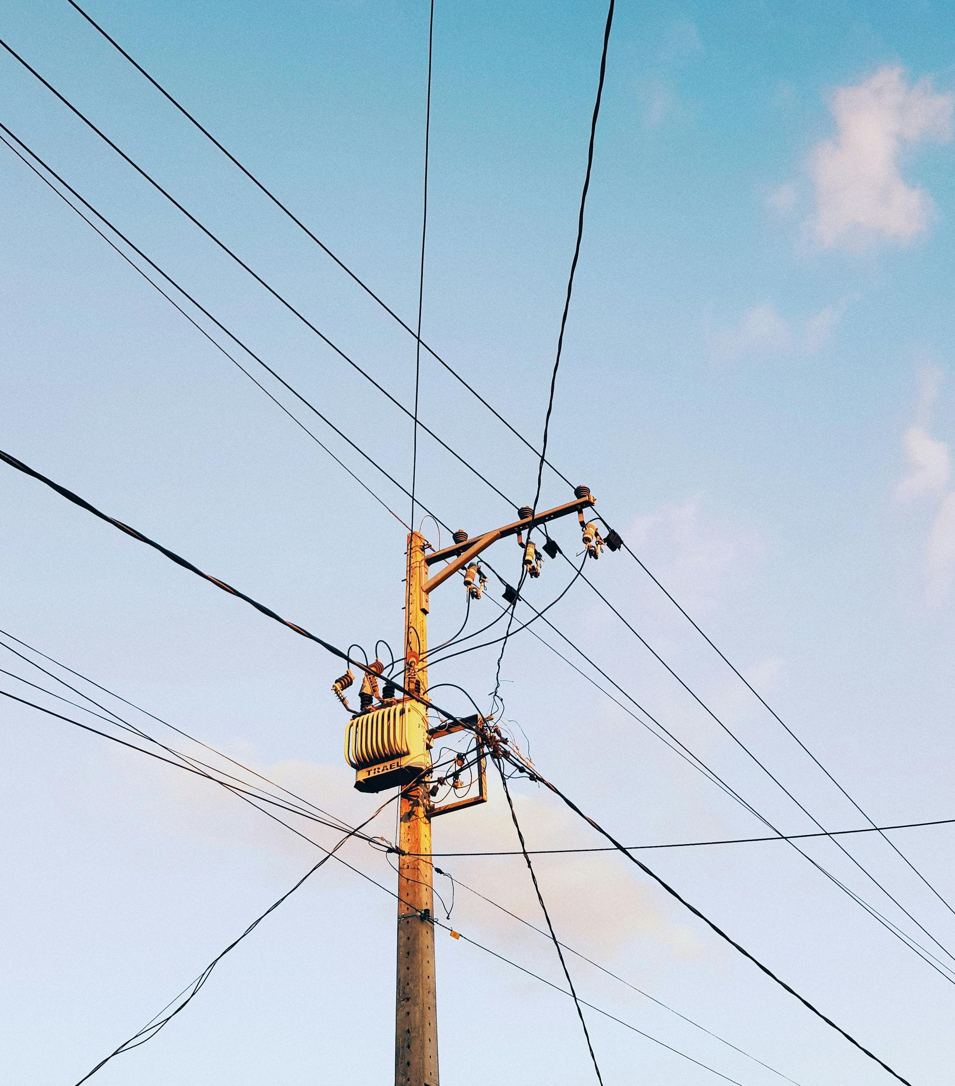 Power lines on a yellow utility pole against a blue sky. A yellow transformer is attached to the pole.