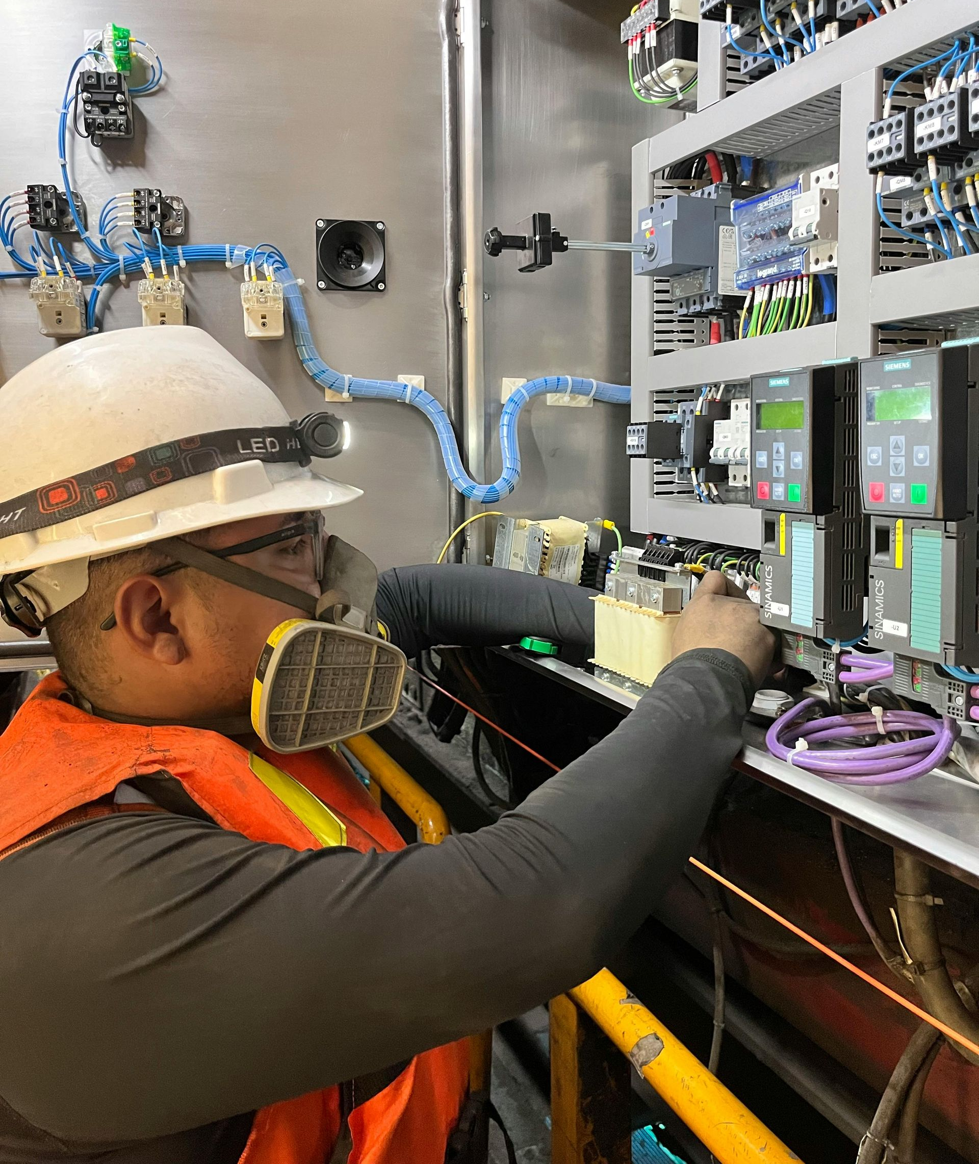 Electrician in safety gear works on electrical panel.
