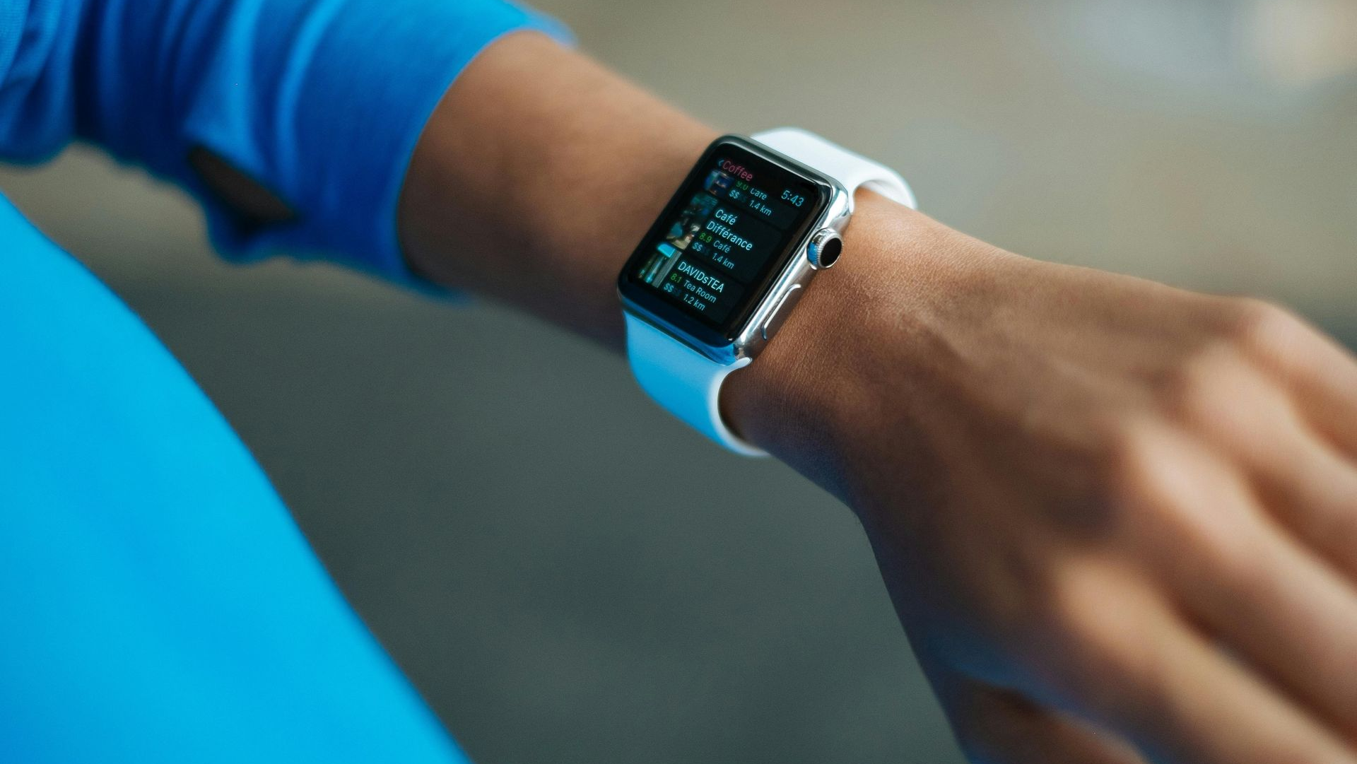 Wrist with white smartwatch, blue shirt, showing data on screen.
