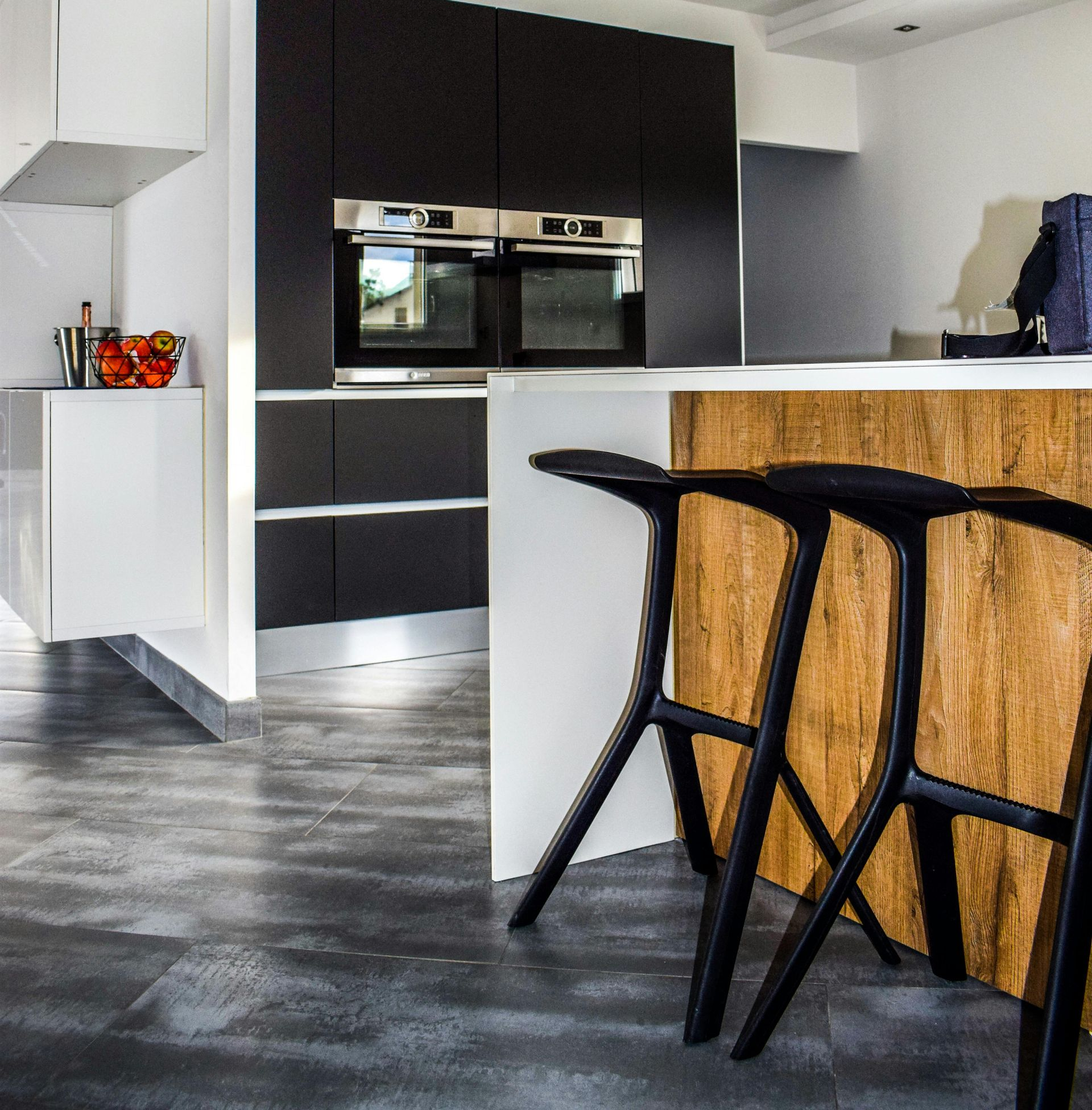 Modern kitchen with black and white cabinetry, wood accents, and bar stools.