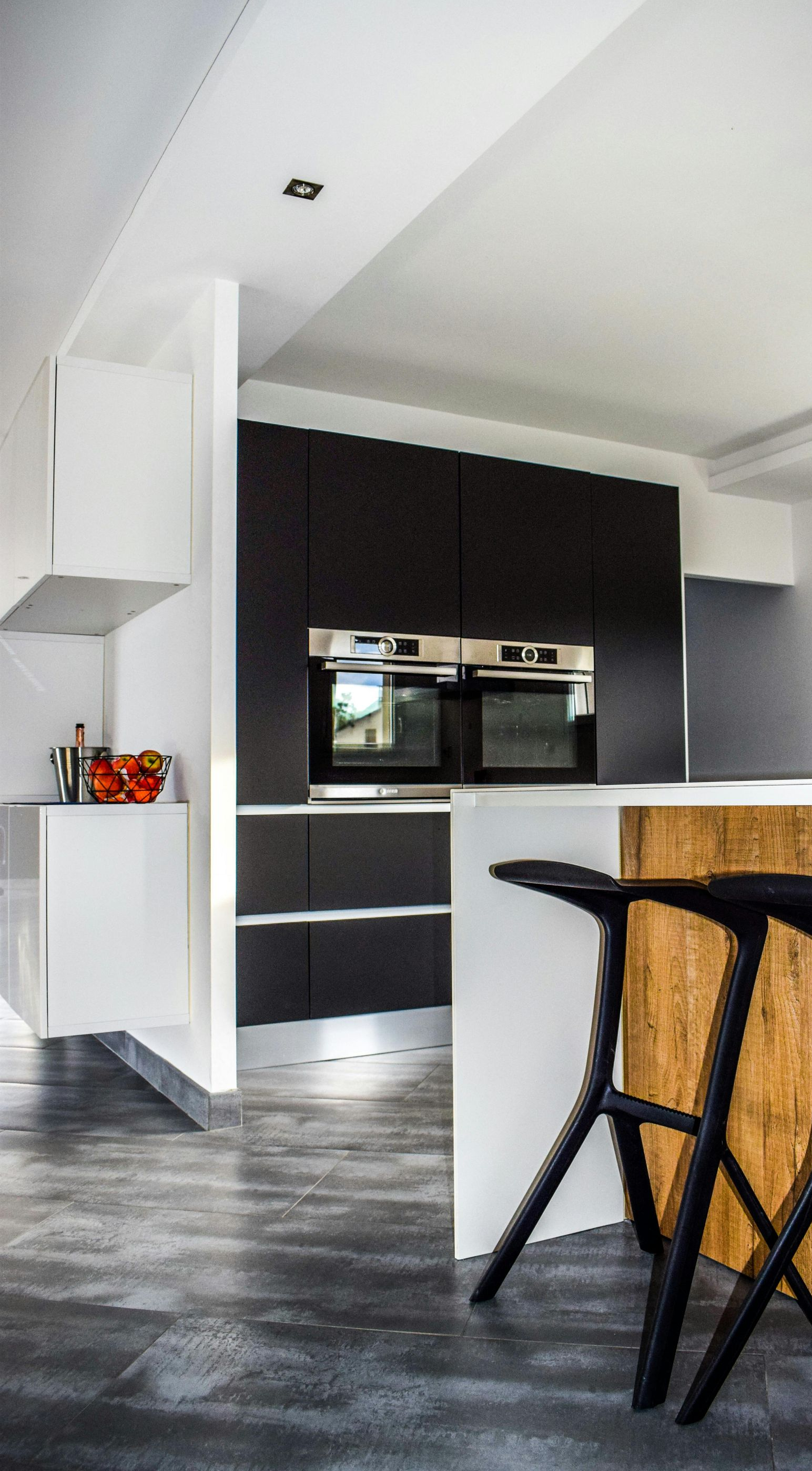 Modern kitchen with black and white cabinetry, a wood-paneled island, and black bar stools.