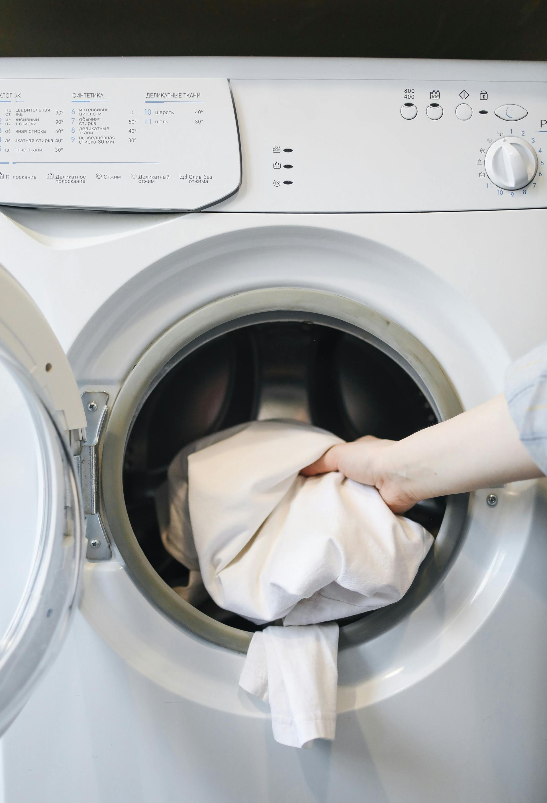 Person placing white fabric into an open washing machine.