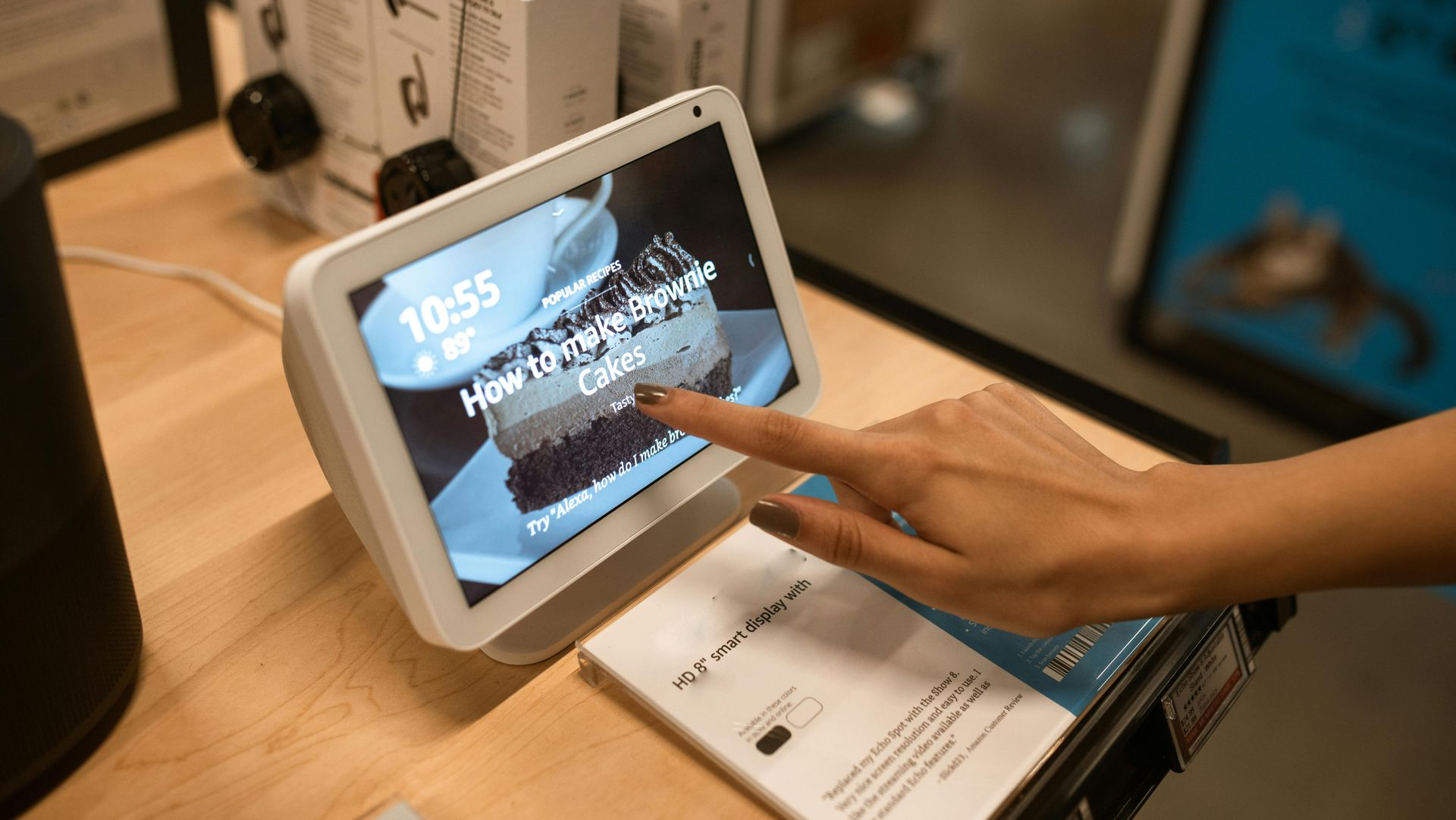 A person interacting with an Amazon Echo Show screen displaying a cake recipe, in a store setting.