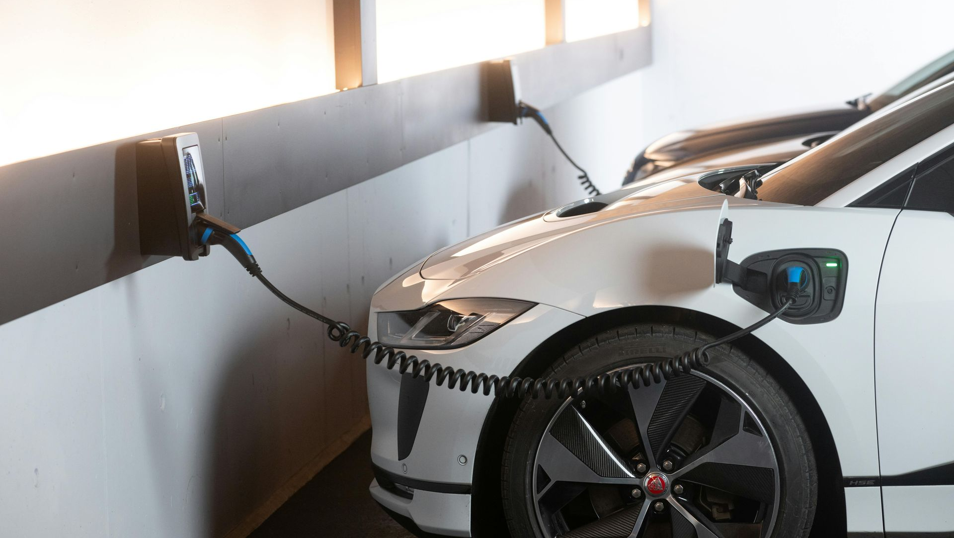 White electric car charging in a garage; charging cable connected to the car and wall charger.