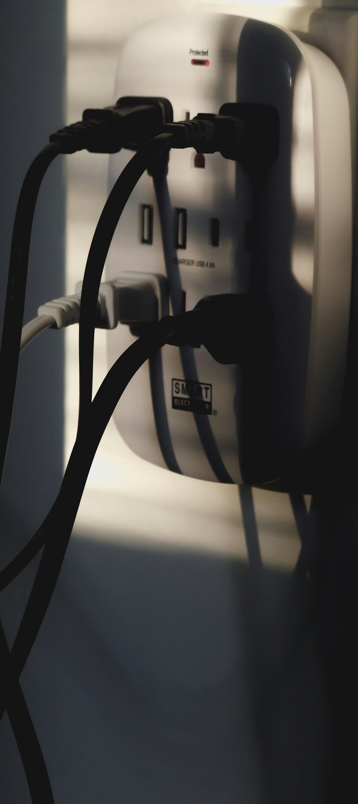 Close-up of a wall-mounted power strip with multiple cords plugged in, casting shadows.