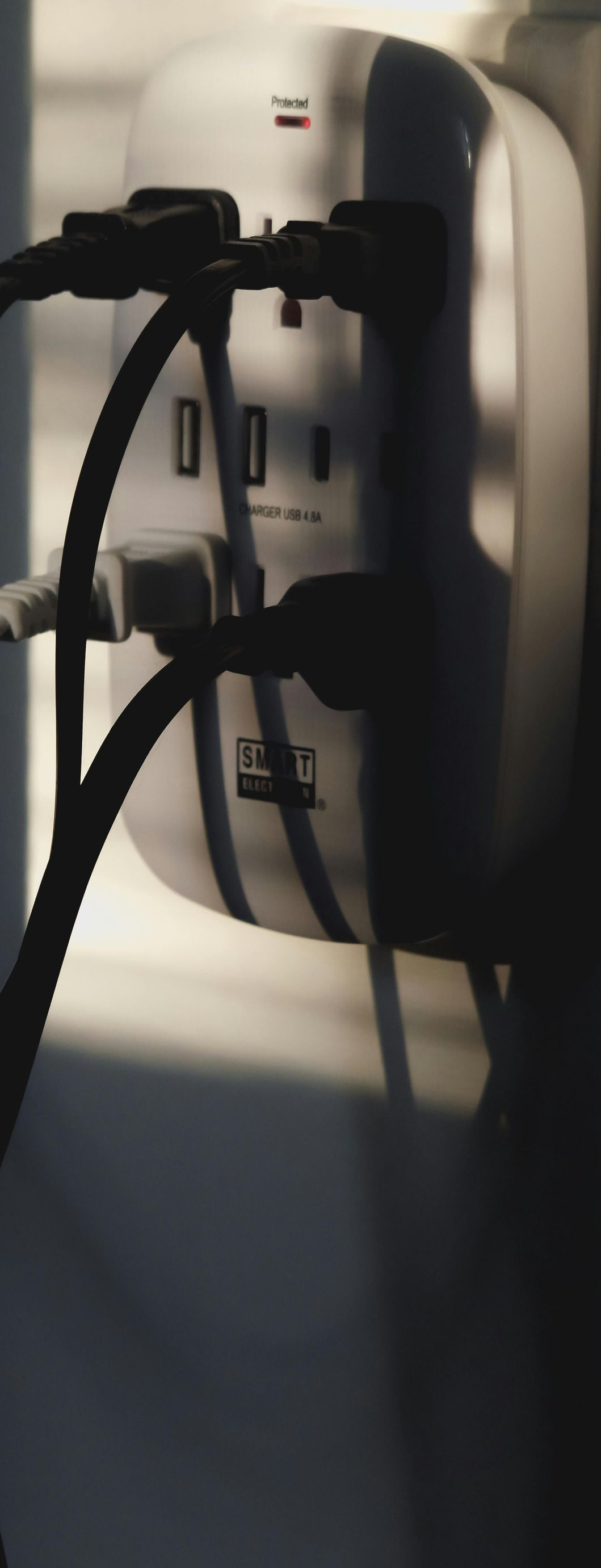 Power strip with multiple outlets and USB ports, plugged in with black cords, set against a white wall.