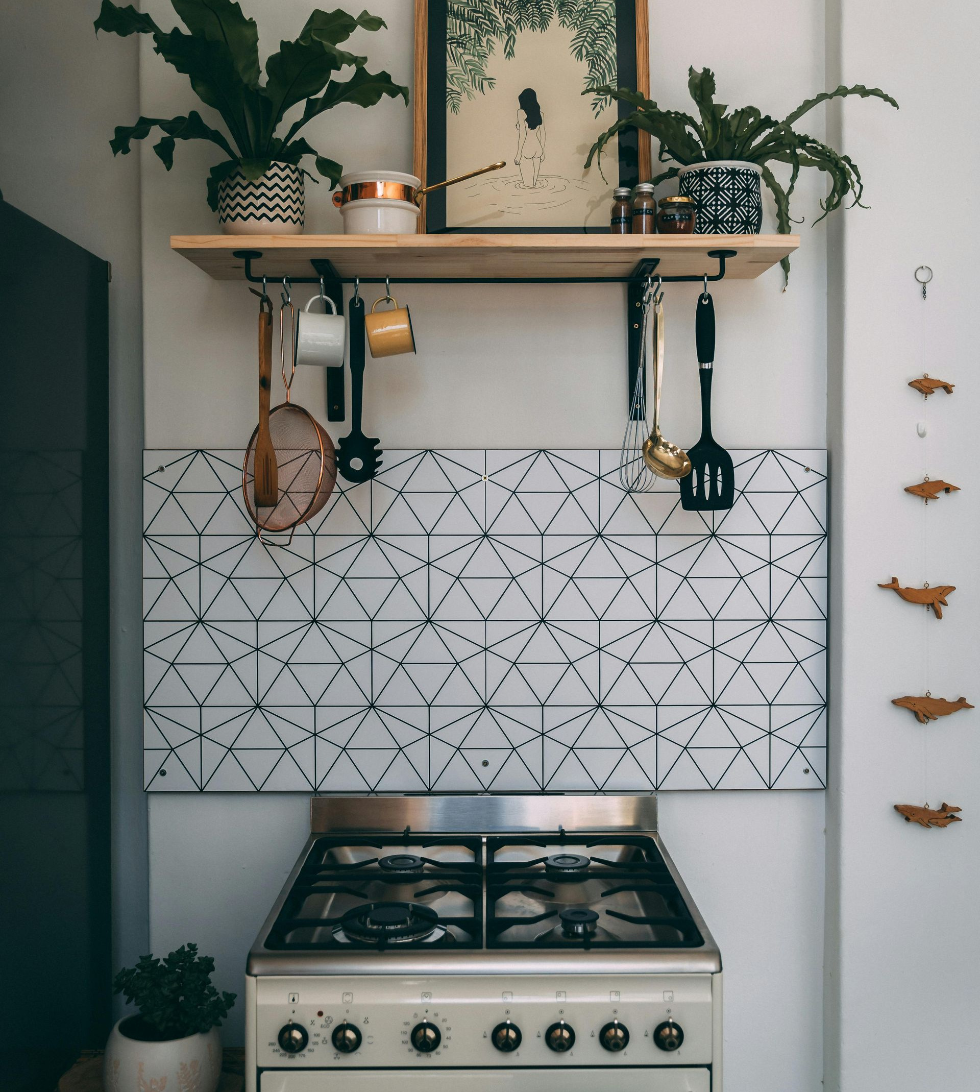 Kitchen with patterned backsplash, shelf with plants and utensils, above a stove.