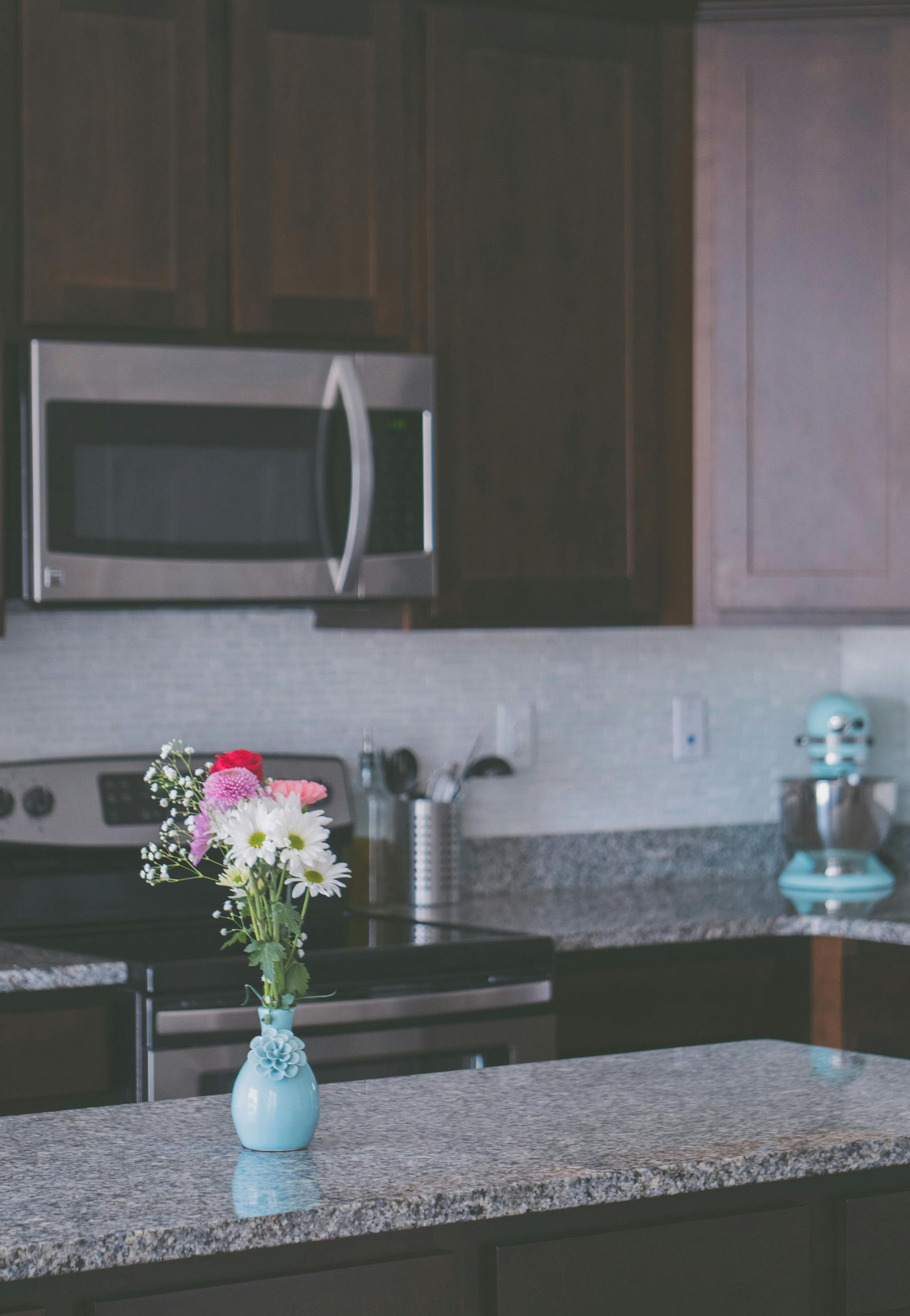 Kitchen interior with flowers in a vase on granite countertop, stainless steel appliances, and dark cabinets.